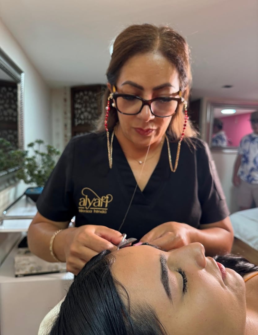 Woman threading another womans eyebrows in a salon setting.