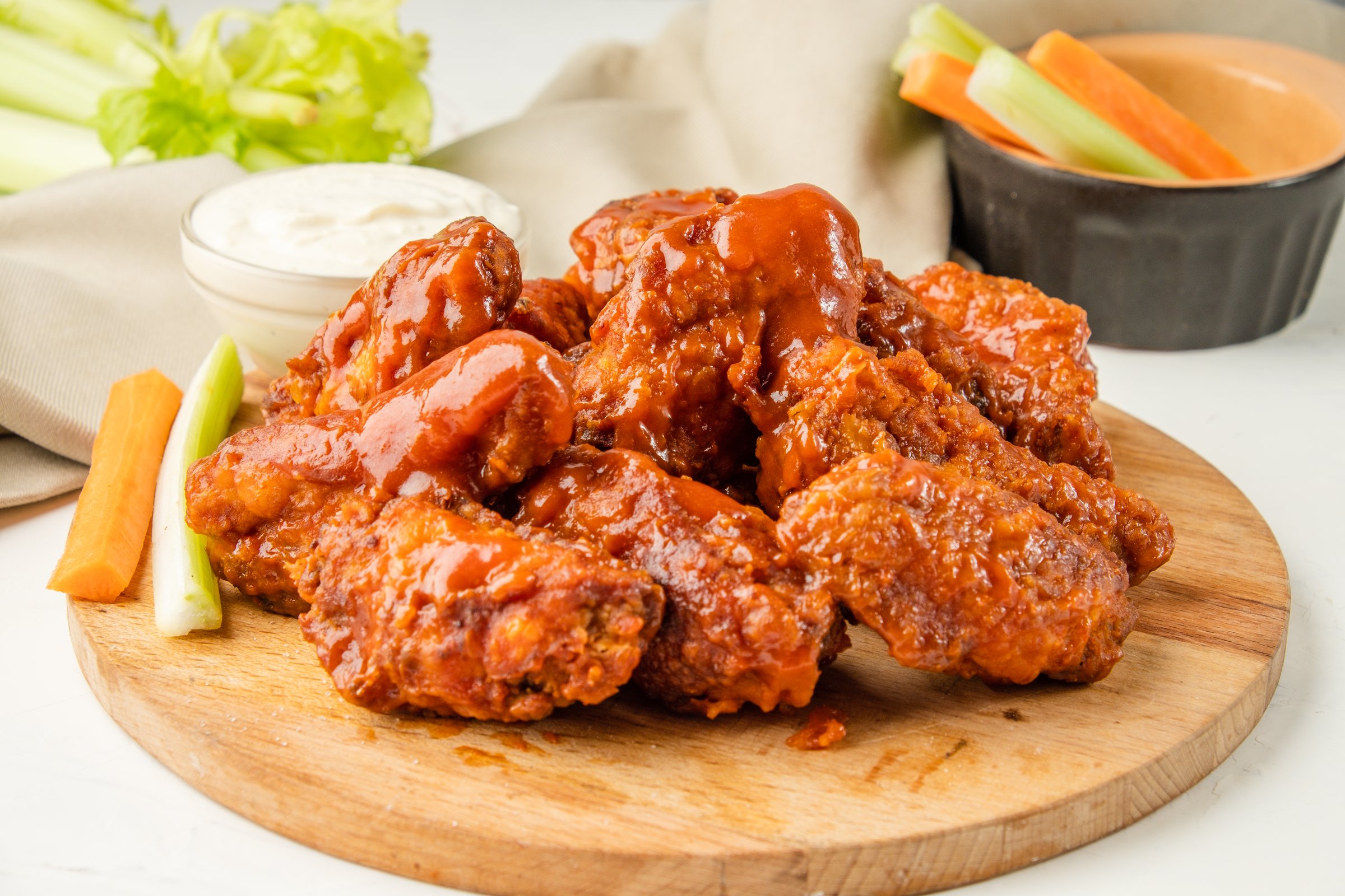 Fried bbq wings a lot, served on a wooden board with celery and carrot vegetables and blue cheese sauce. Traditional buffalo wings.