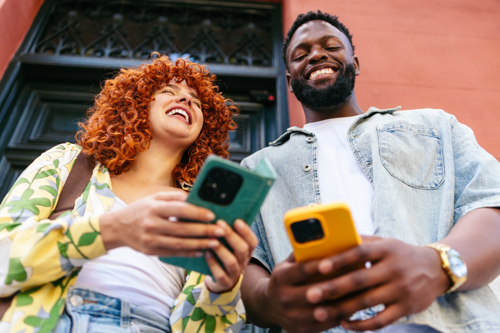 Two happy friends are using smartphones and laughing at something funny they're watching together on the screen