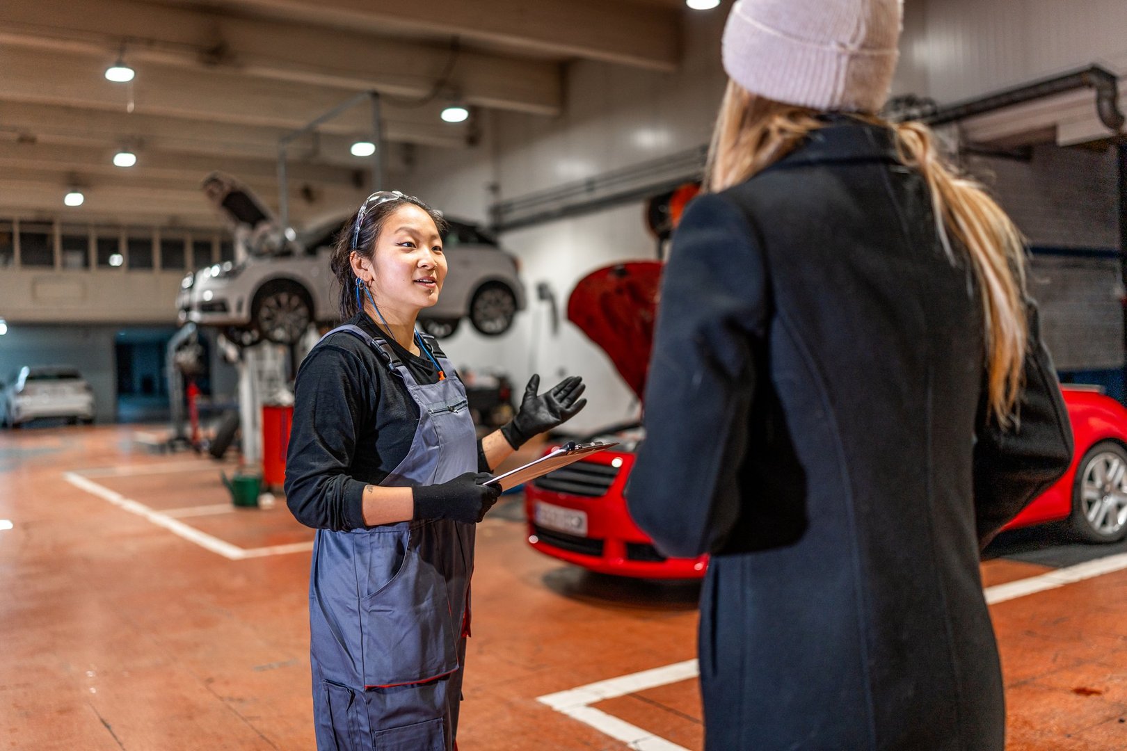 Professional female mechanic explaining car repair details to customer, holding clipboard in auto repair shop