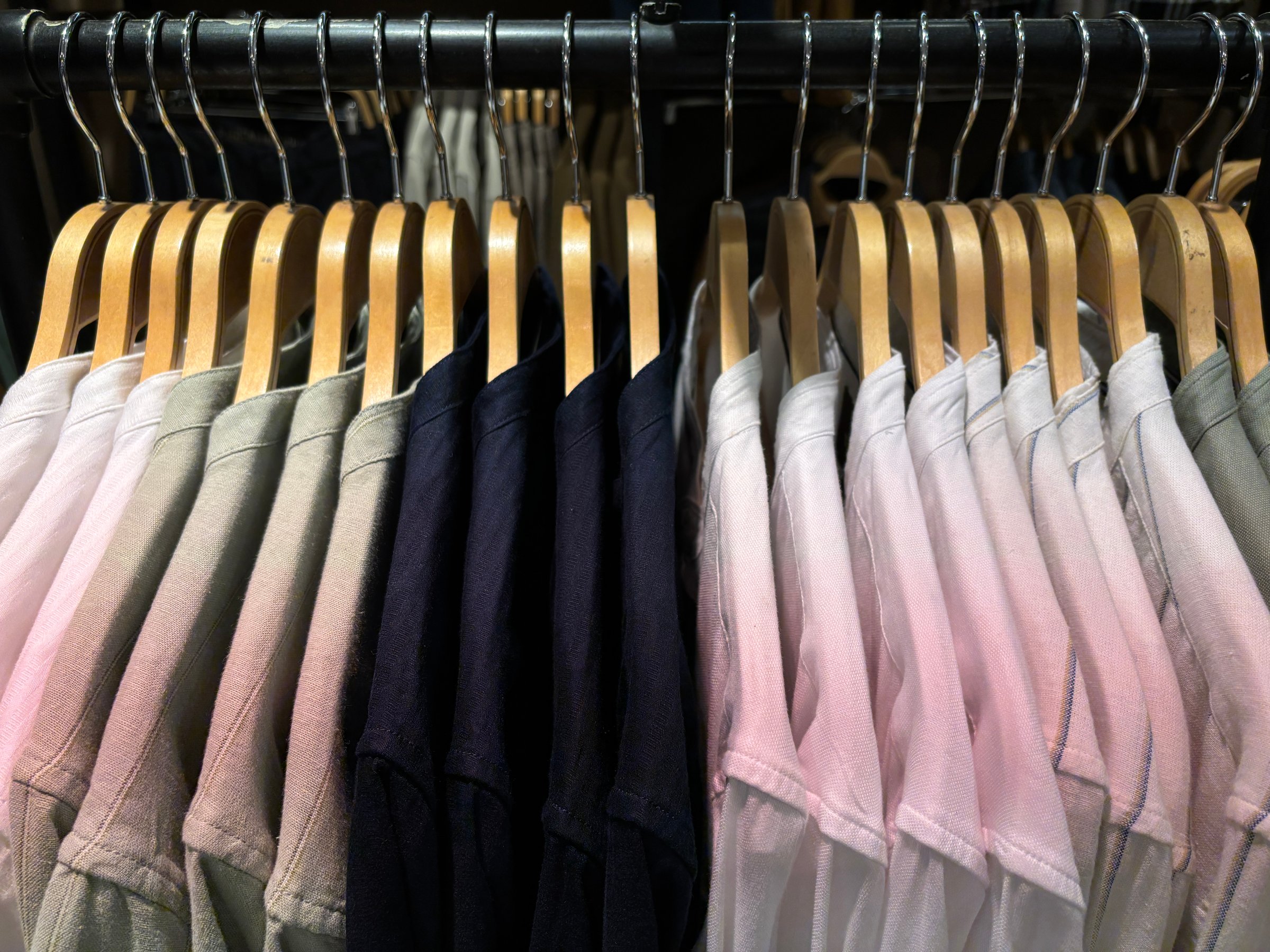 Neatly arranged shirts on wooden hangers in a clothing store, showcasing a gradient of soft neutral tones