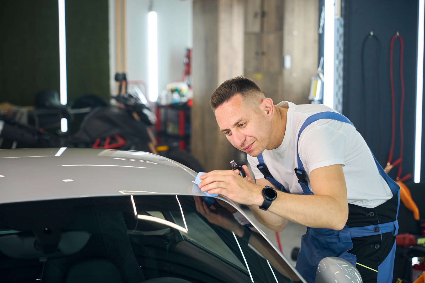 Master wipes the car body with a soft sponge, a man in work overalls