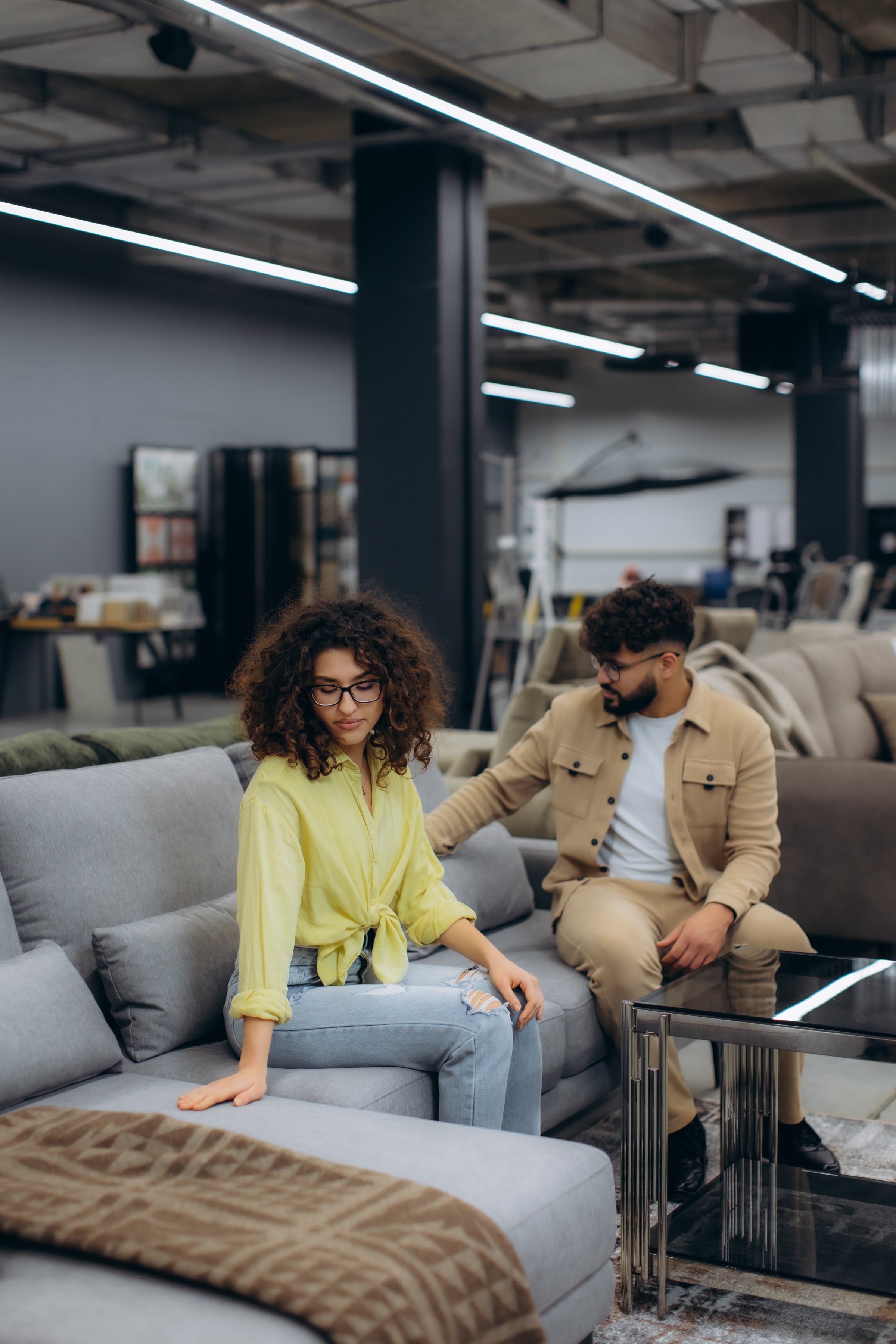 Couple trying out a grey sofa in a large furniture showroom, making decisions for their new home interior design