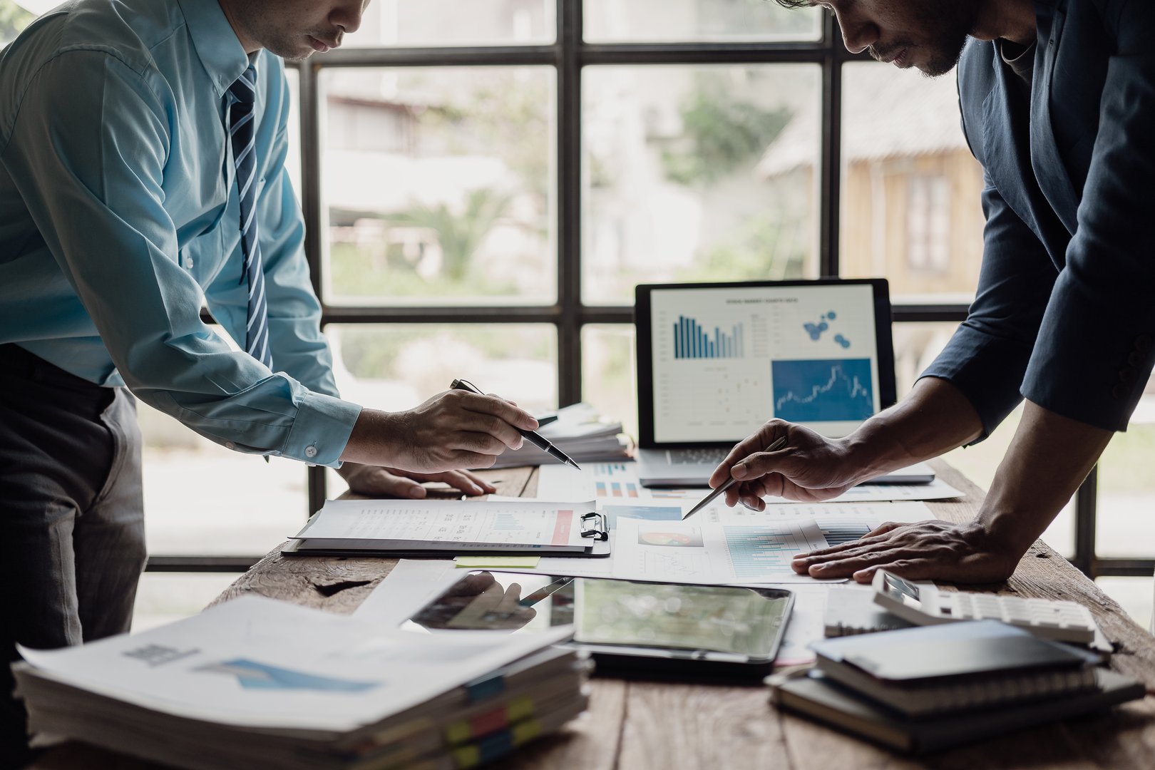 Two businessmen analyze statistical financial data on laptops, pointing at screen with growing graphs and charts, talking about company growth and solving financial problems. For small businesses