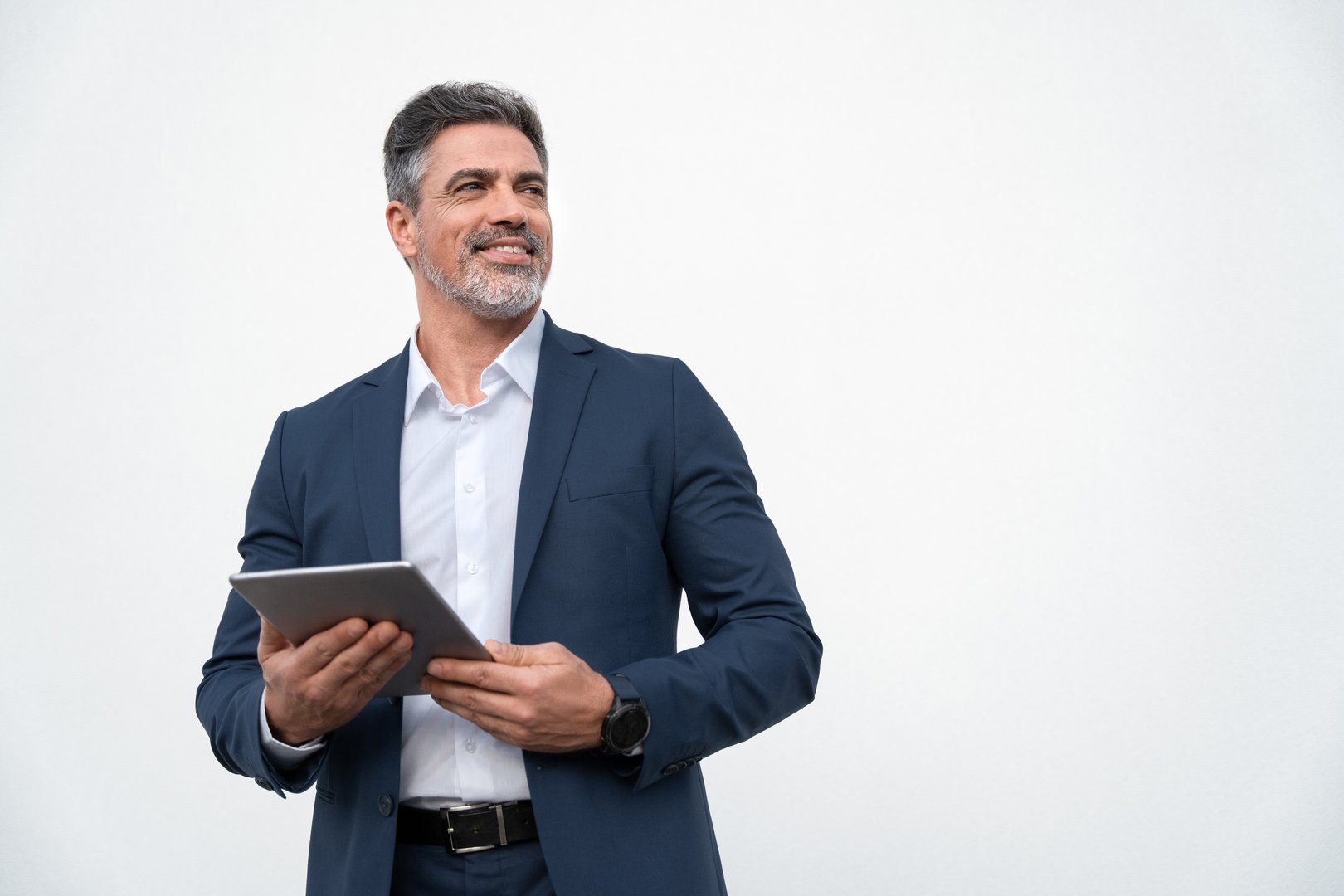 Middle age mature businessman using pc tablet for business work application. Smiling handsome older man in formal suit holding touchscreen device looking aside. Isolated white background, copy space