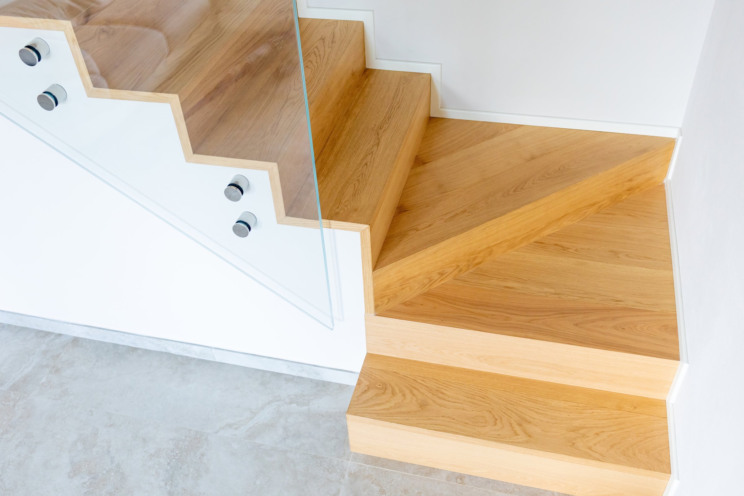 Modern and minimalist oak staircase featuring a sleek glass balustrade, enhancing the bright and clean design of a contemporary home with elegant architectural elements