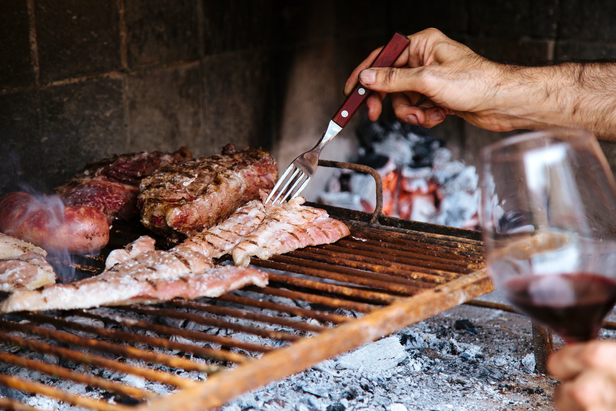 Man with a red wine glass making a barbeque, bbq meat cooking on grill. Traditional Asado of Argentina, Paraguay y Uruguay.
