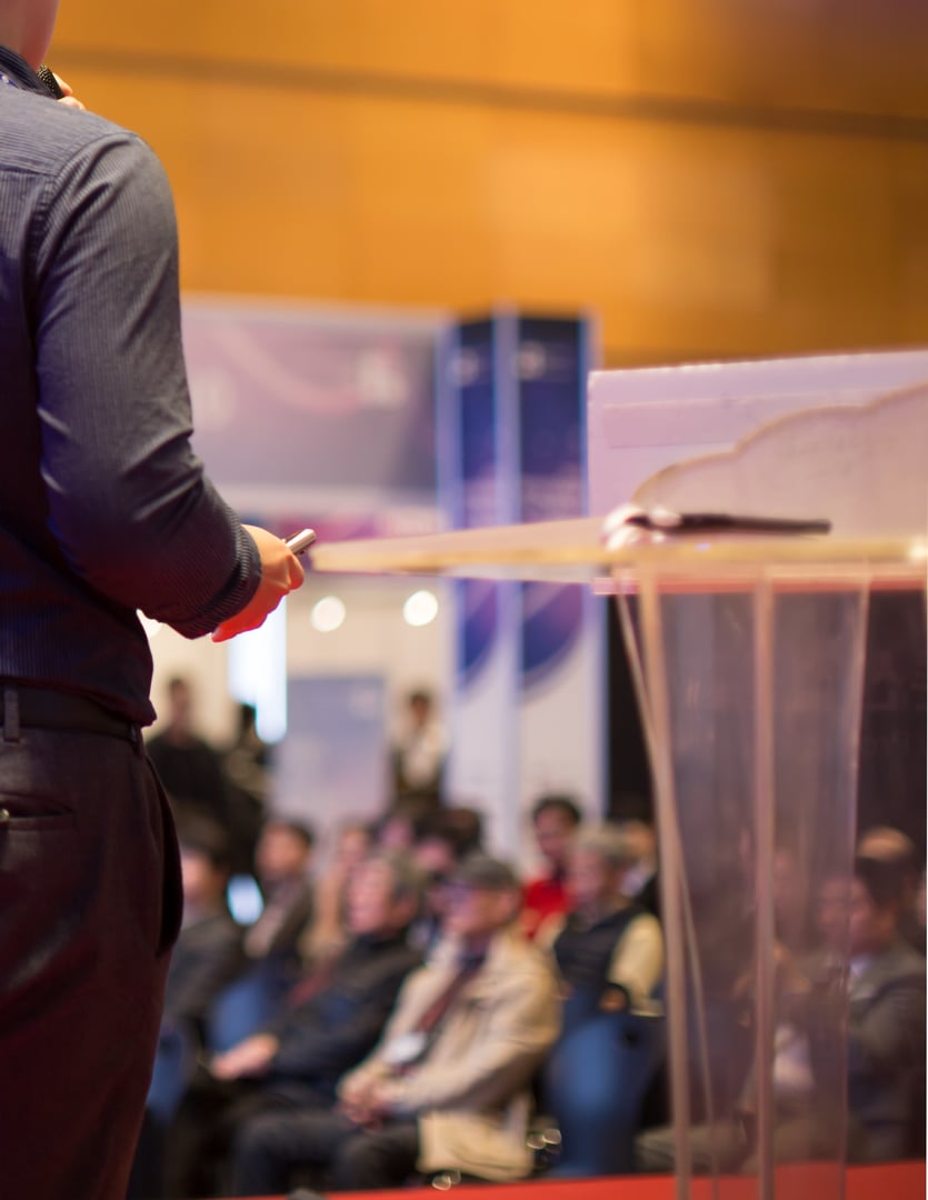 Hand Holding Projector Remote Control Next to Podium