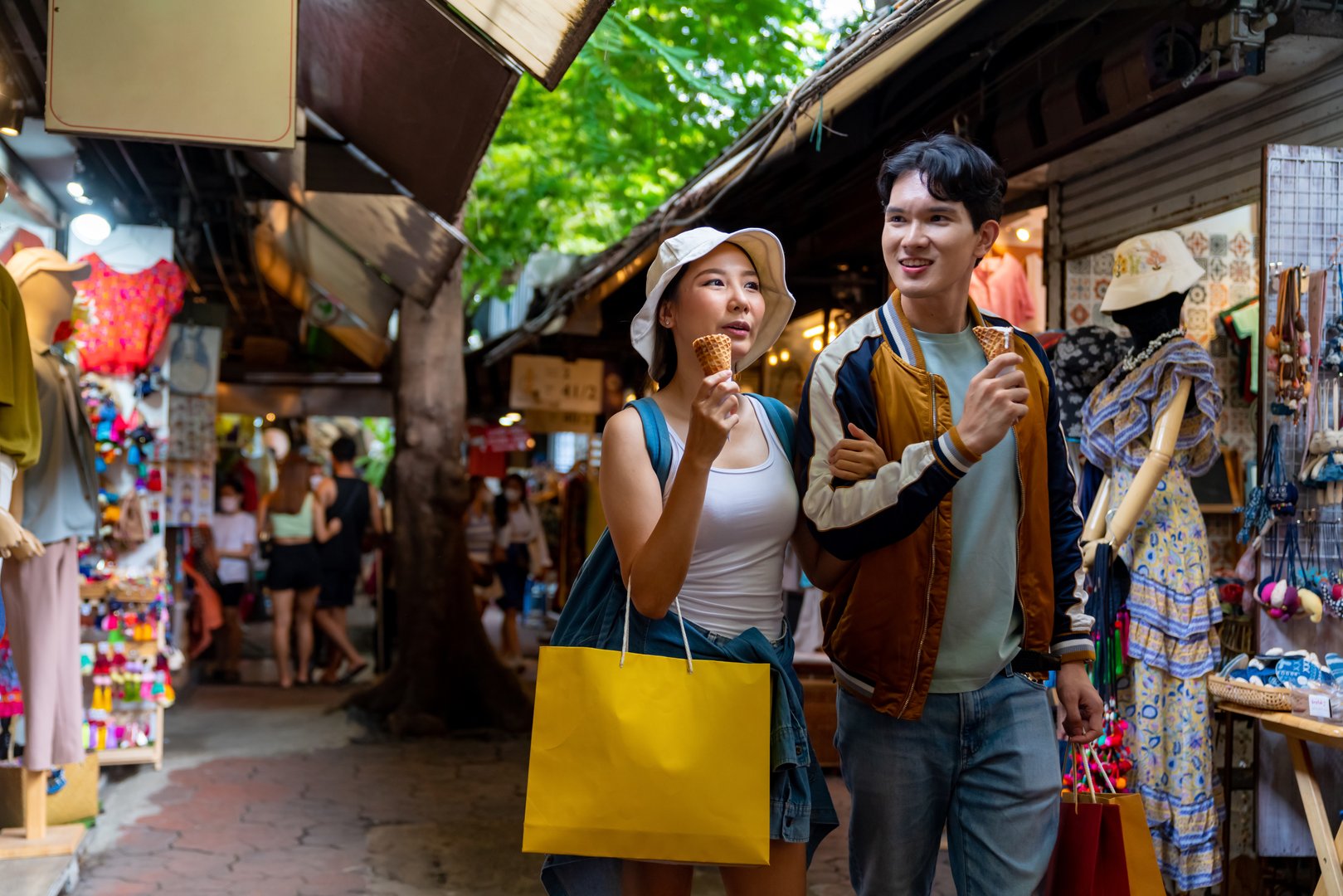 Young Asian couple enjoy and fun outdoor lifestyle shopping at street market on summer holiday vacation. Man and woman couple eating ice cream cone while walking and shopping at weekend street market.