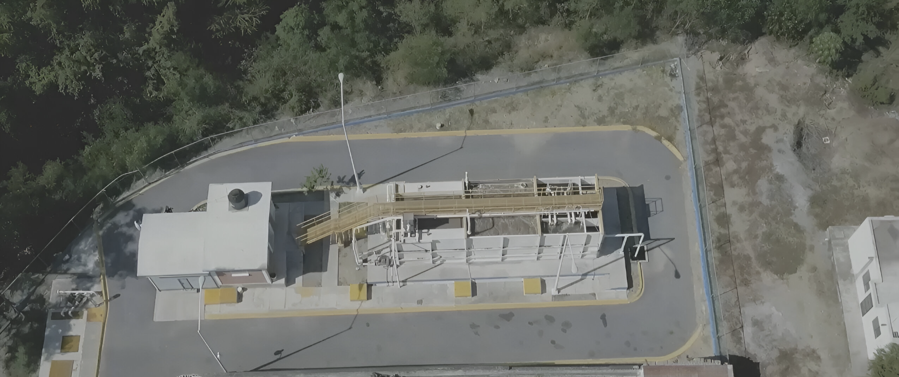 Aerial view of a small industrial facility with rectangular structures, piping, and surrounding greenery.