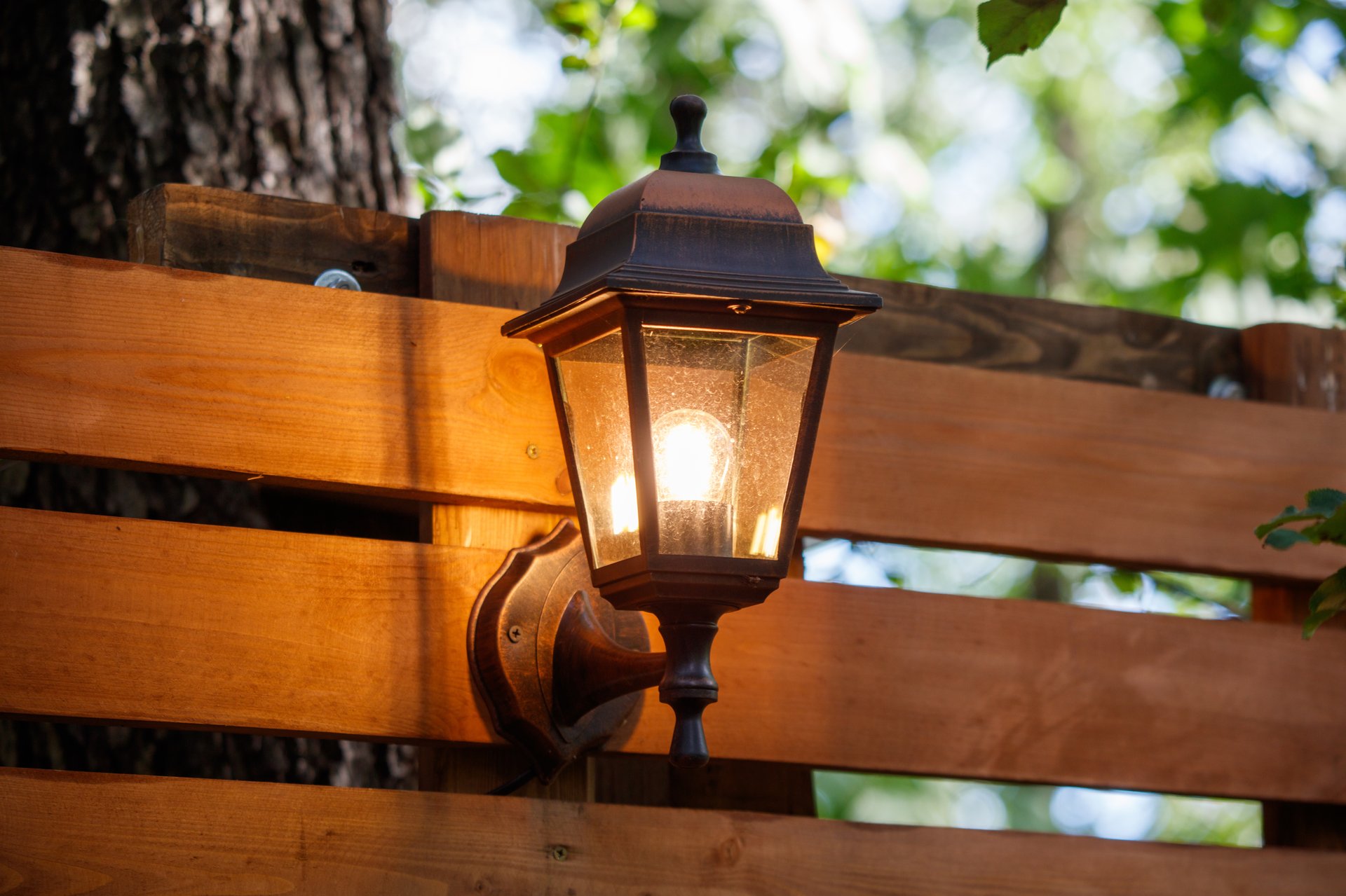 A lighted lamp post is on a wooden fence.