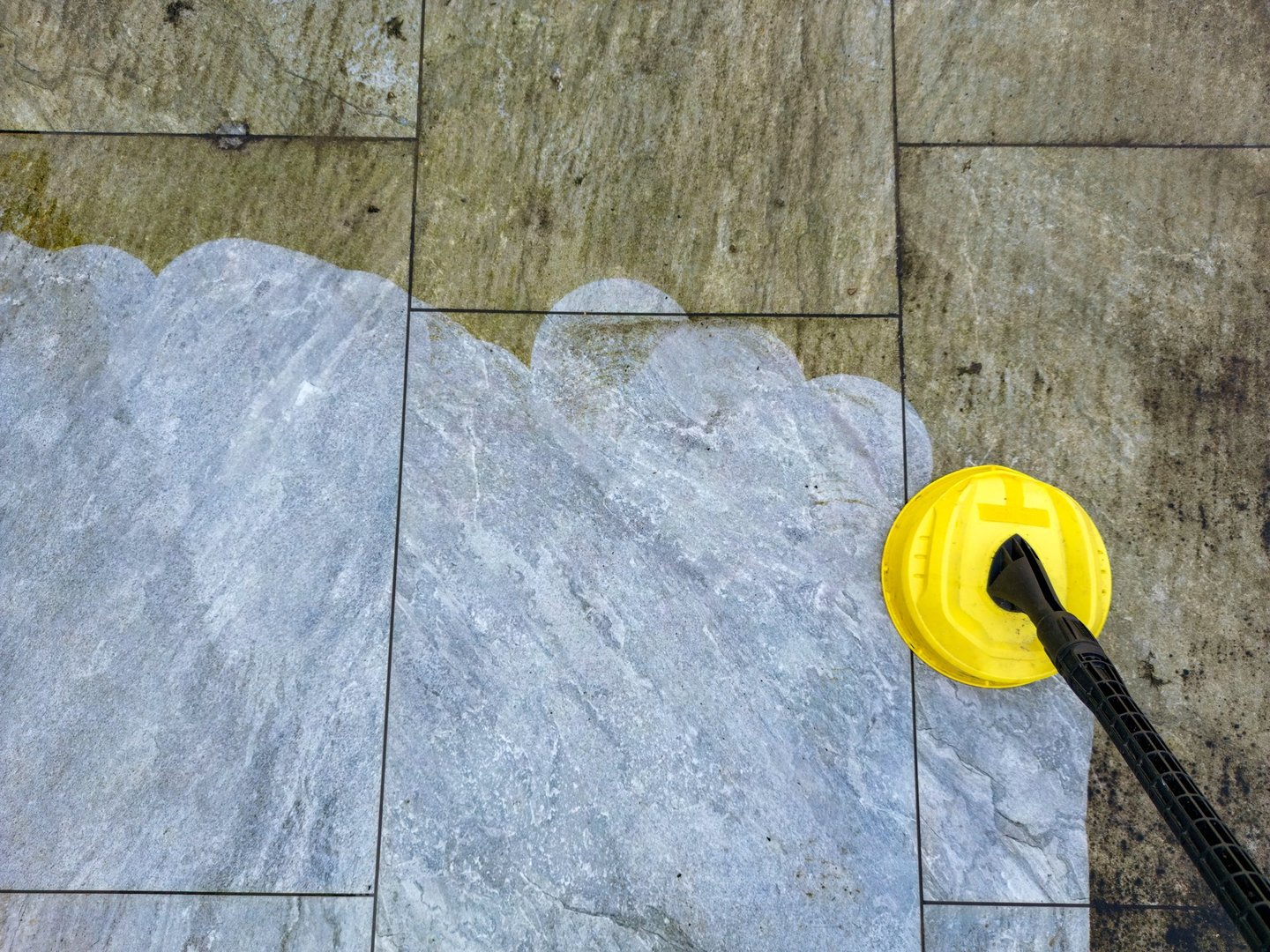 Pressure jet washer being used to clean porcelain tiles on a garden patio showing the difference before and after cleaning