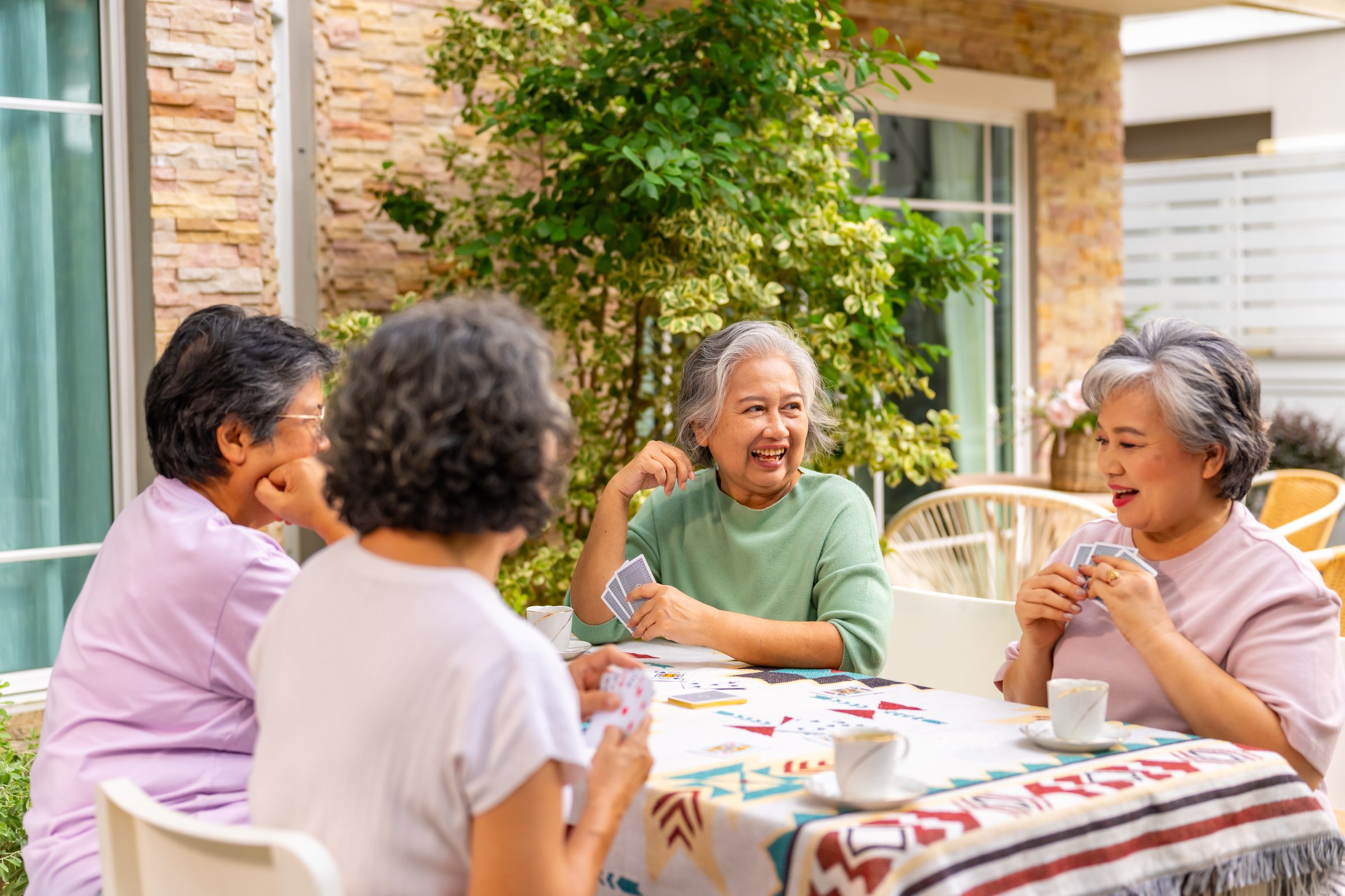 Group of Happy Asian senior mature women relax and enjoy indoor lifestyle meeting party together at home. Elderly retired woman friends having fun playing card together at home garden in summer day.