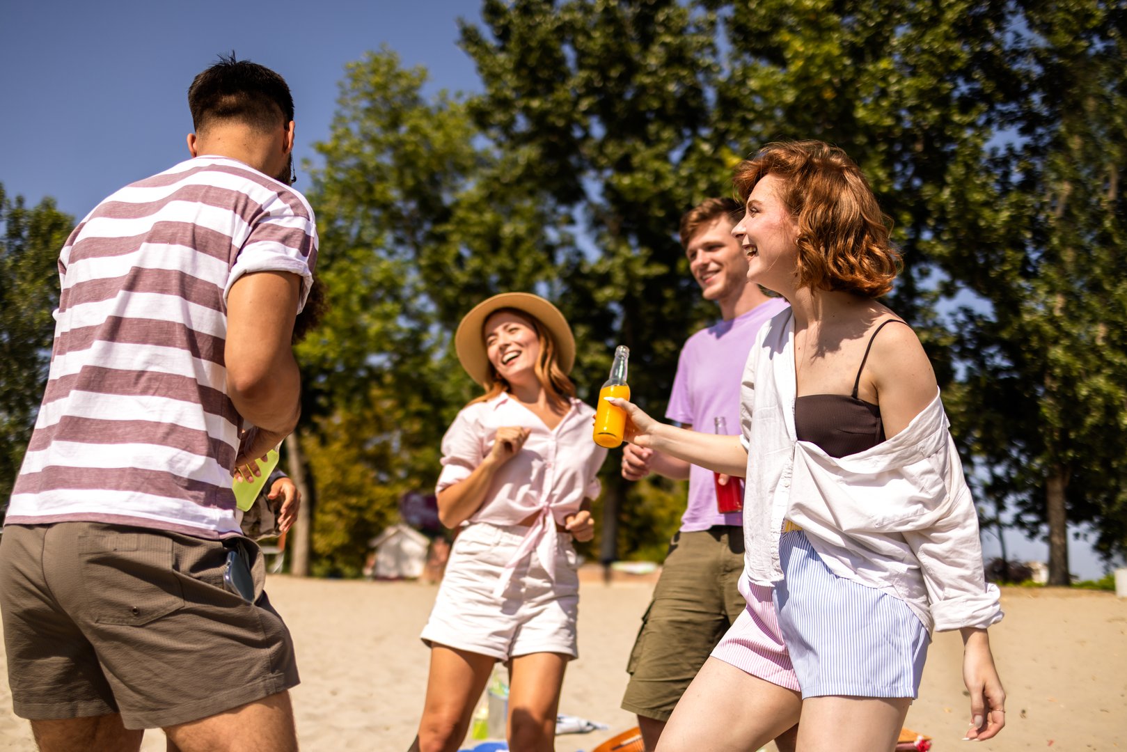 Group of multiracial friends dance at the beach while they drink cocktails and listen to music.