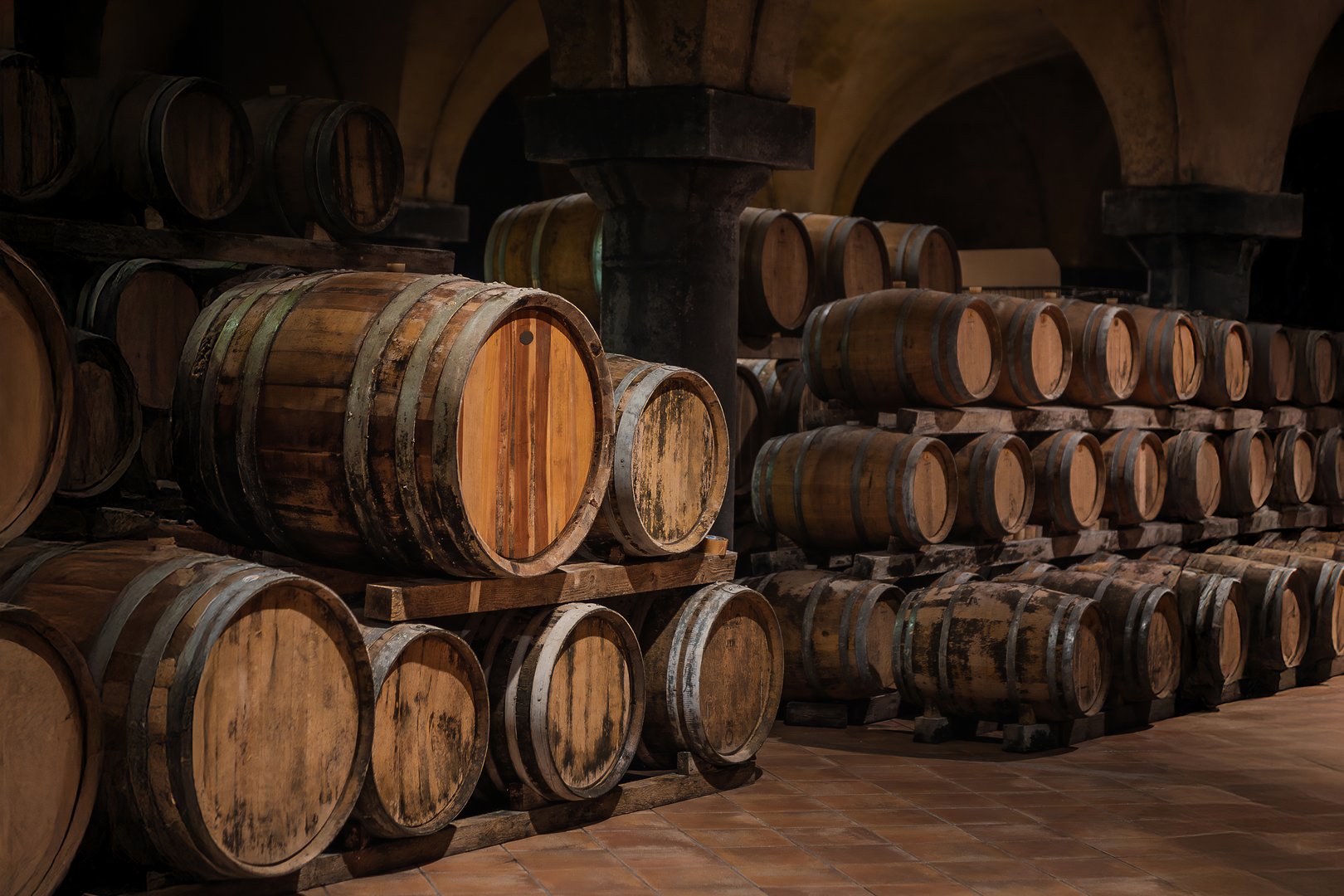 Traditional cellar with stacked wood barrels. Rustic environment with vaults. Red wine or whisky aging. Warm professional atmosphere. Traditional winemaking mood.