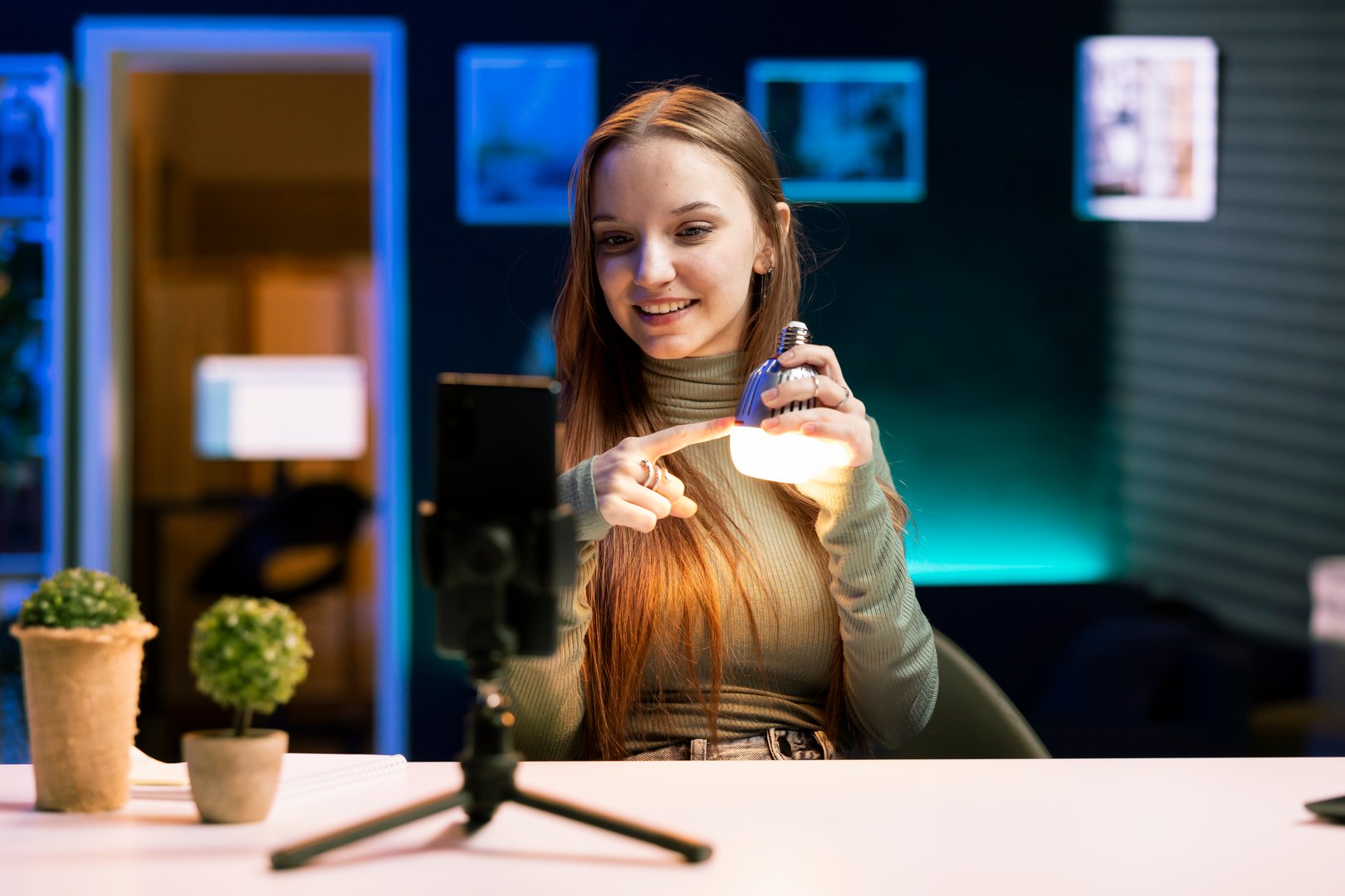 Happy girl doing house improvement video vlog, filming newly launched smart light bulb with phone. Smiling entertainer greeting fanbase, presenting WIFI home automation, recording with smartphone