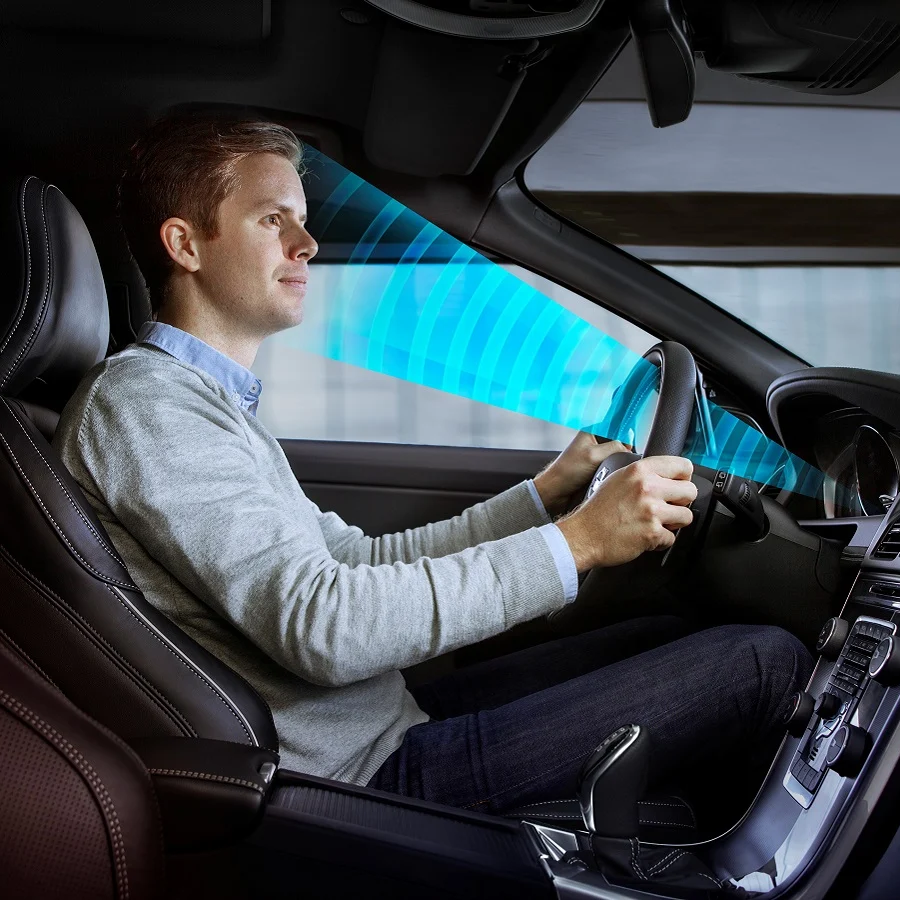 Man driving a car, focused on the road, with a blue sensor grid projected on the windshield.