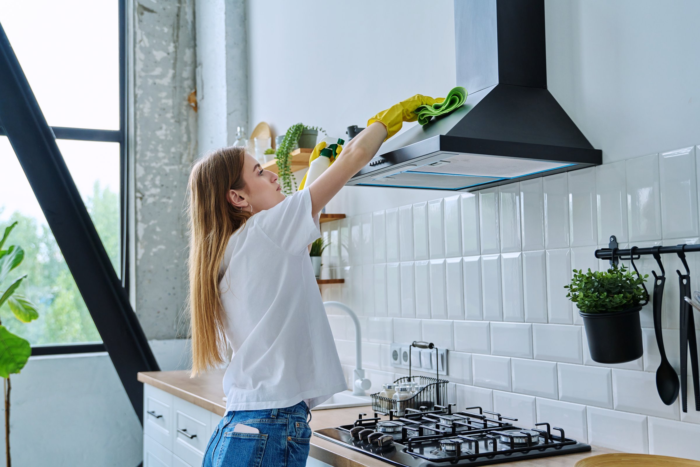 Young woman in rubber gloves cleaning kitchen, washing surface of hood above stove with rag. Cleanliness, hygiene, housework, lifestyle, home concept