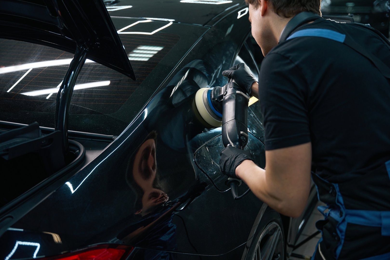 Back view of car detailing professional buffing rear quarter panel with polisher