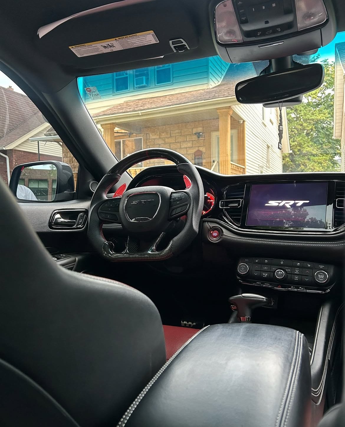 Interior of a modern car with black and red accents, showcasing a steering wheel, dashboard, and digital display screen.