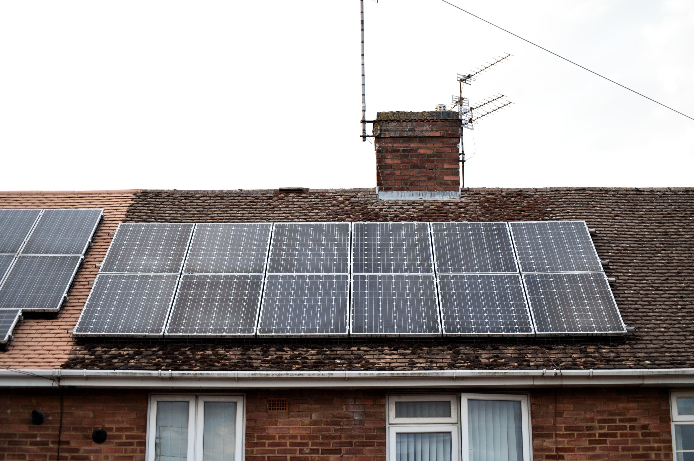 Wide view of solar panels mounted on the roof of a red brick house in a British residential area, eco-conscious living and energy efficiency.