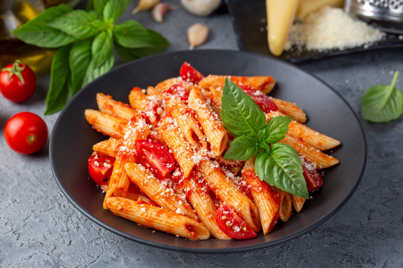 Classic italian pasta penne alla arrabiata with basil and freshly grated parmesan cheese on dark table. Penne pasta with chili sauce arrabbiata.