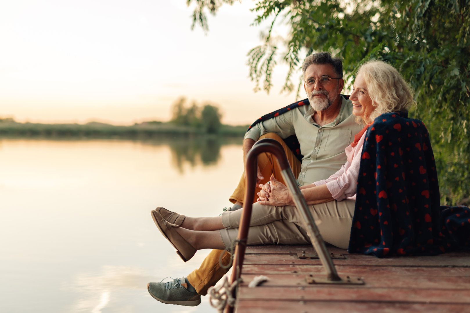 Elderly couple relaxing on a pier, sharing a blanket and enjoying the sunset over the lake