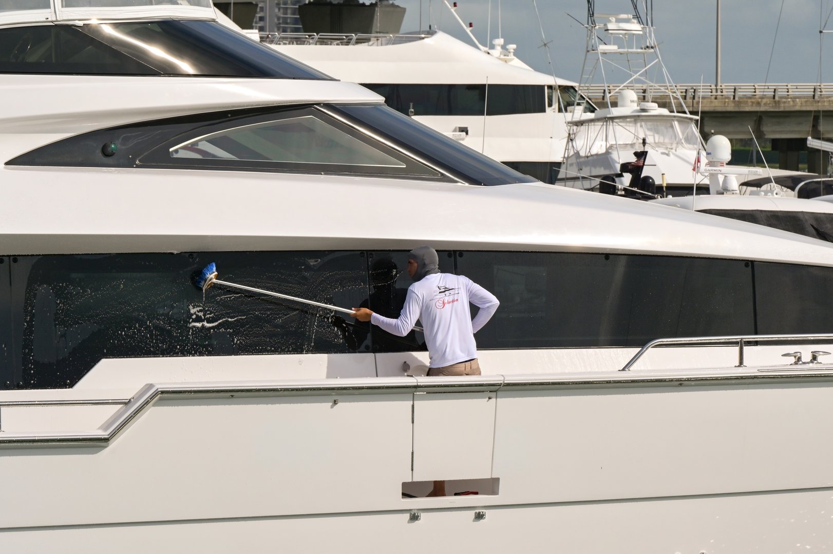 Miami, Florida, USA - 1 December 2023: Crew member of a luxury superyacht cleaning the windows with a brush