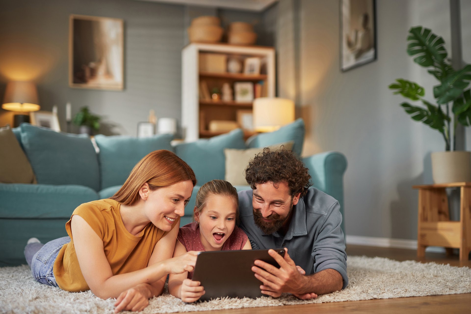 Happy family lying on the floor using digital tablet at home, mother, father and daughter enjoying time together