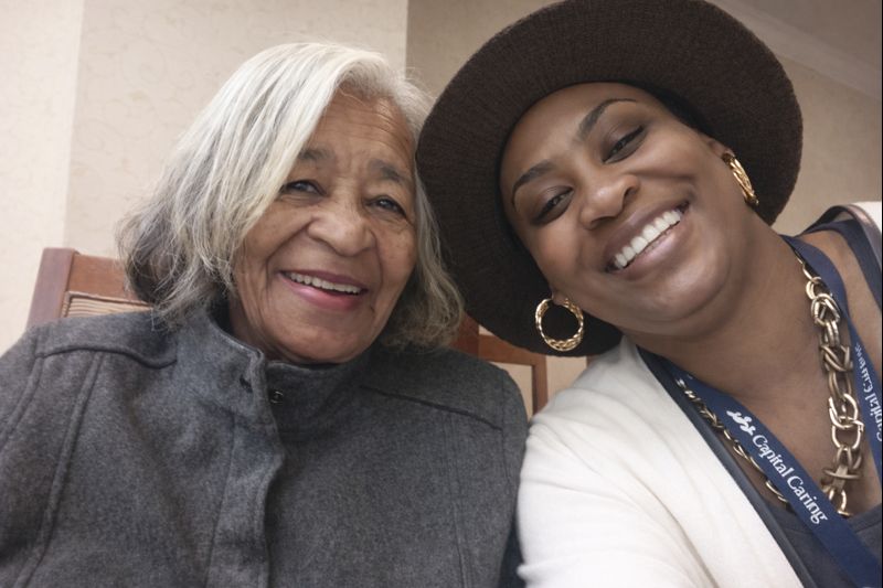 Happy home caregiver assisting her senior patient with walking through the kitchen.