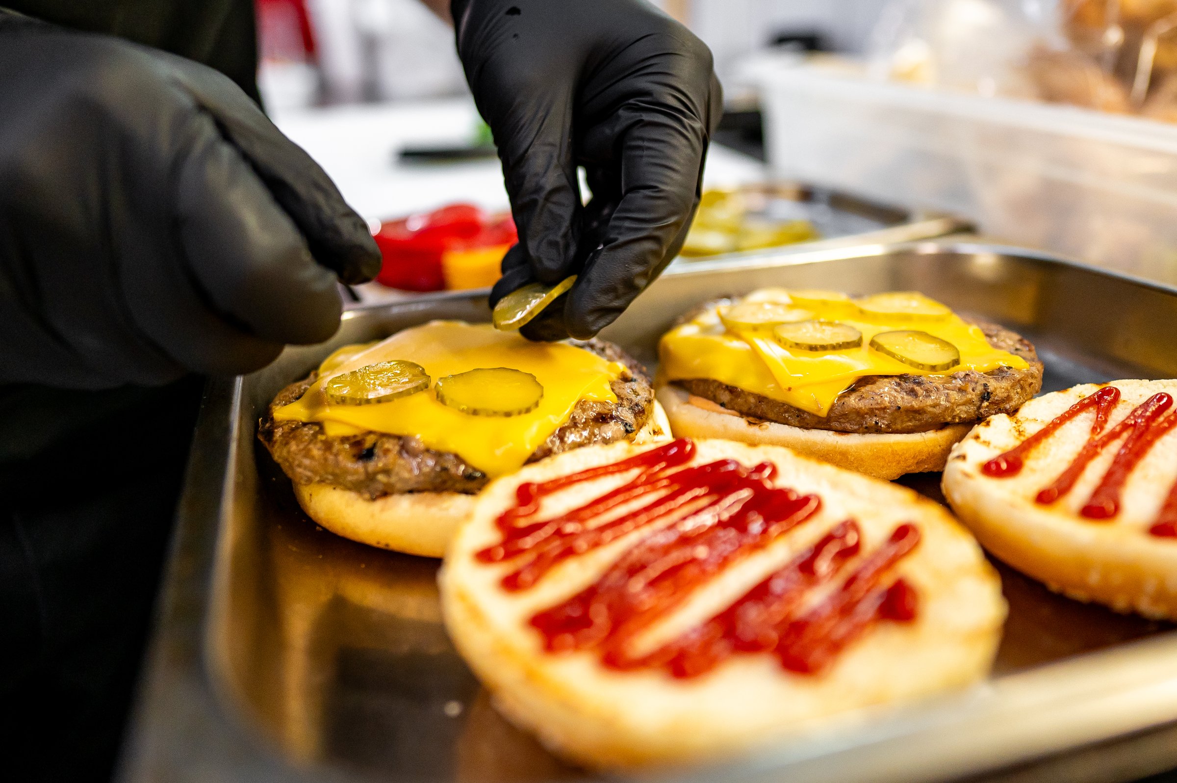 Close-up of hands assembling a freshly prepared cheeseburger with lettuce, tomato, and sesame bun, showcasing fast food preparation