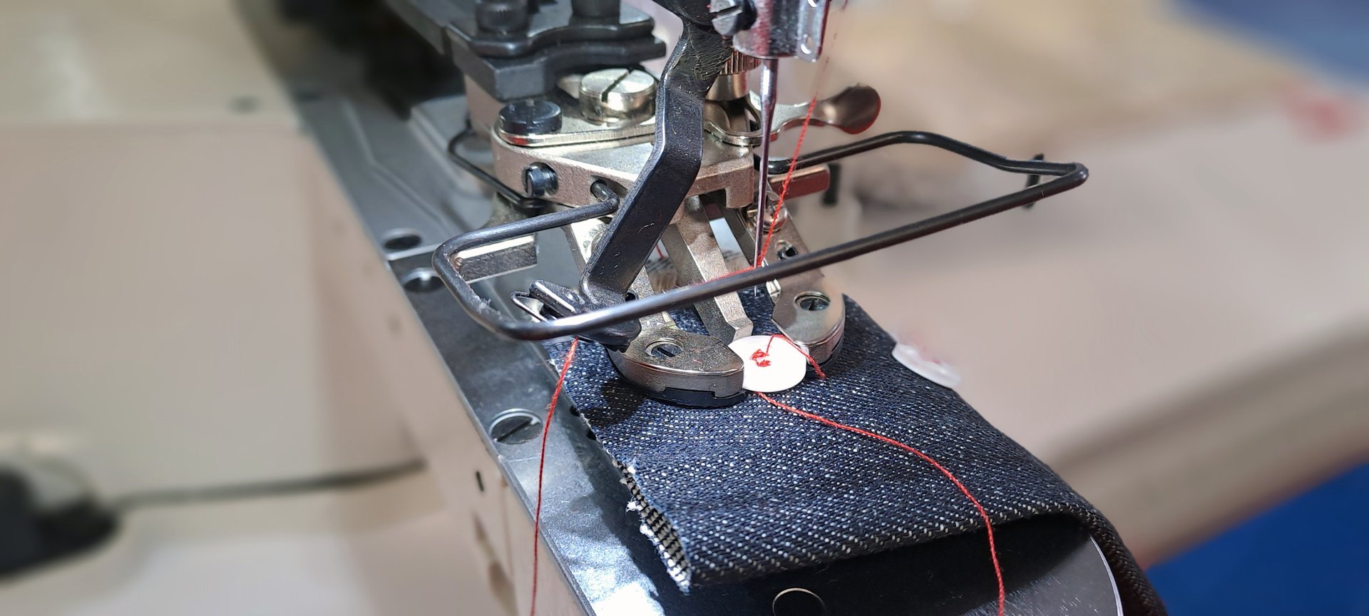 Close-up of sewing machine attaching button to denim, showcasing precision and automation in garment industry