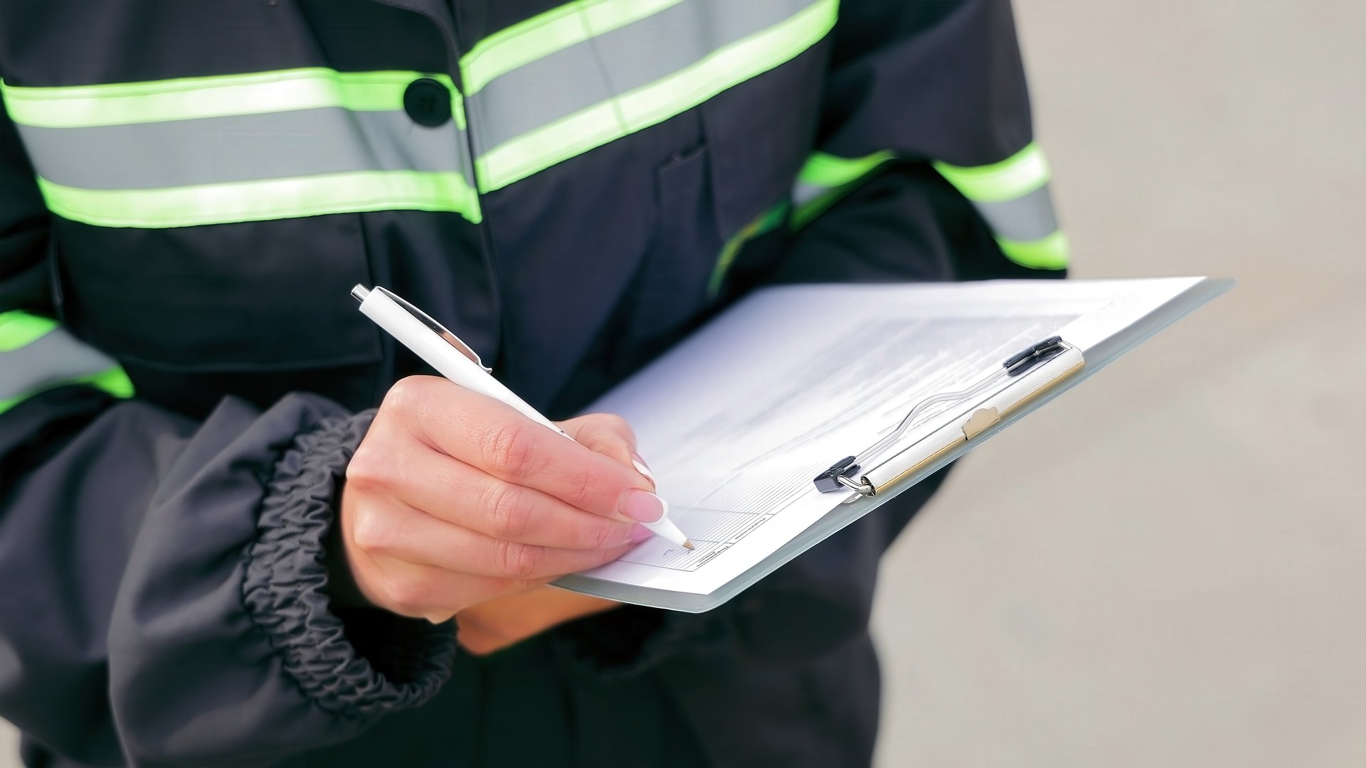 Worker Writing on Clipboard for Inspection. Close-up of a worker in reflective safety gear writing on a clipboard, documenting information during an inspection or checklist process