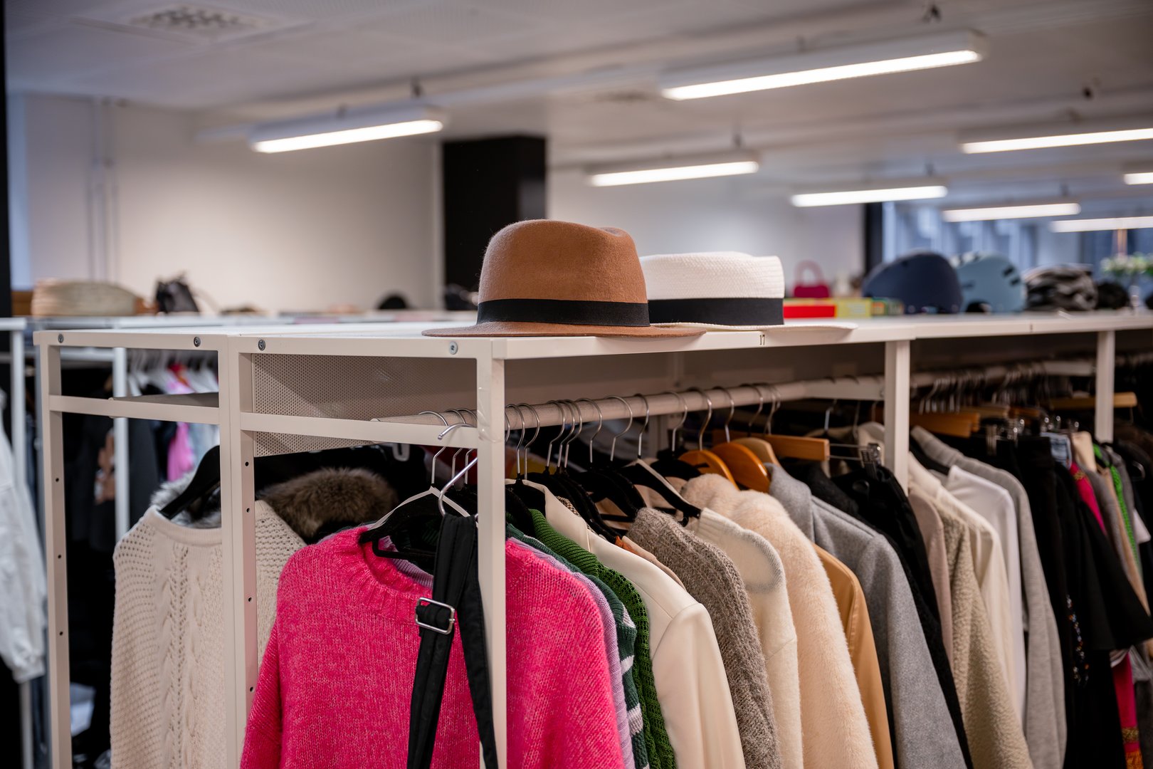 Clothing rack filled with sweaters, jackets, and hats in a thrift store
