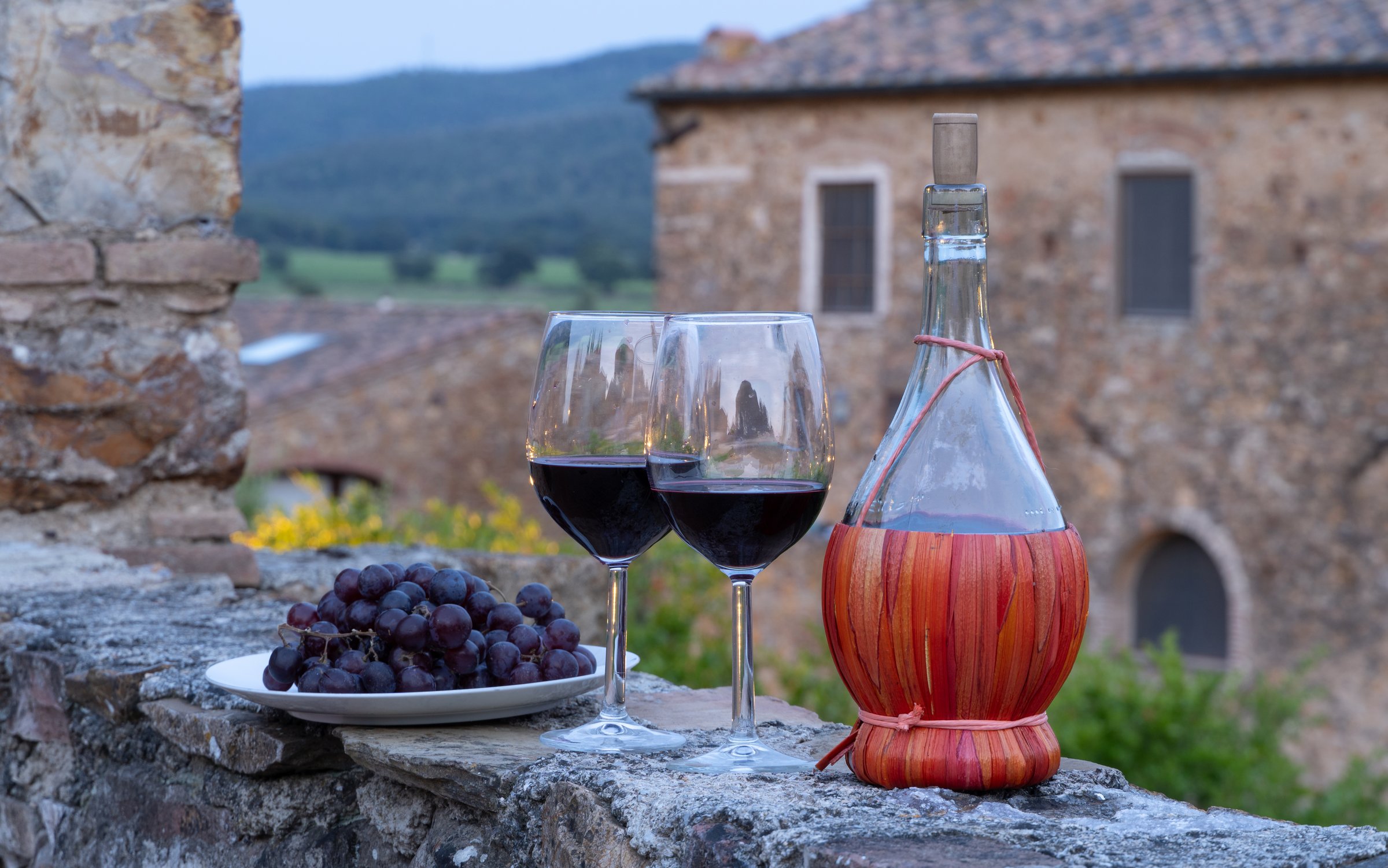 Tow glasses of red wine and typical chianti wine bottle Fiasco against the backdrop of the Tuscany landscape