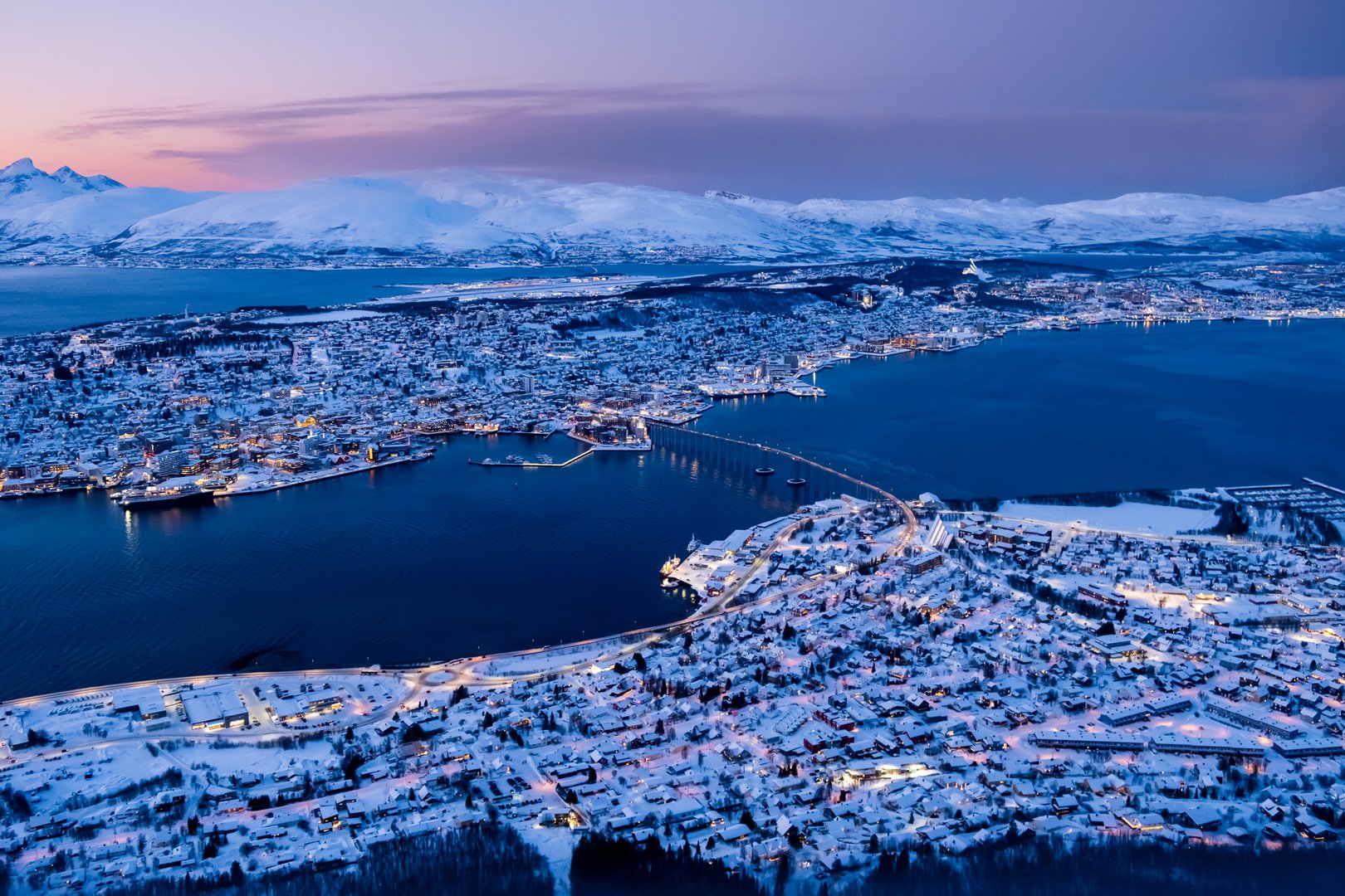 Aerial view of Tromso, Norway with city lights in winter from Storsteinen mountain at twilight. Tromsoya island with Tromso downtown, harbor, Sandnessundet bridge, fjord and mountains in polar night.