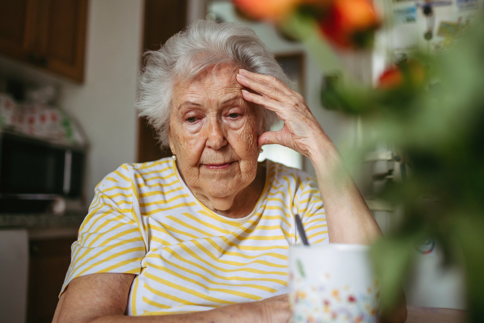 Portrait of worried senior woman crying in kitchen, covering face.