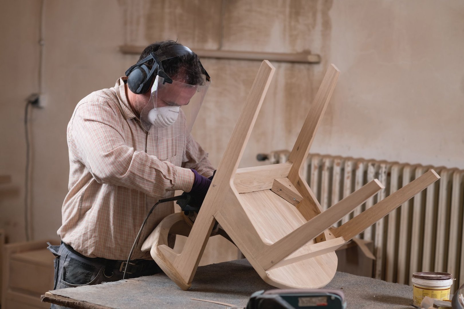Making furniture. Carpenter sanding wooden chair with grinder in furniture factory