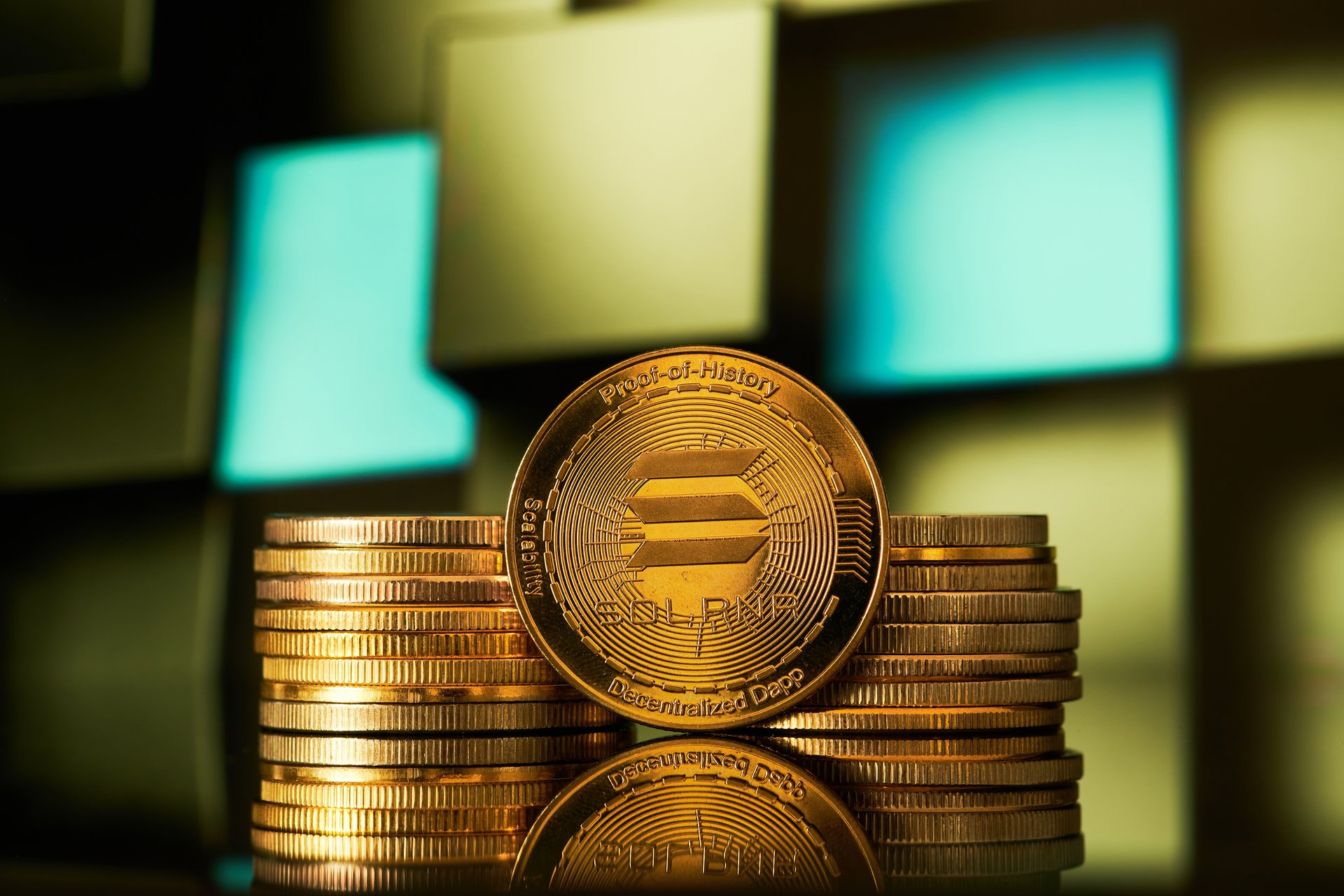 Several golden solana cryptocurrencies are arranged in a pile, reflecting off a surface with a geometric pattern in the background.