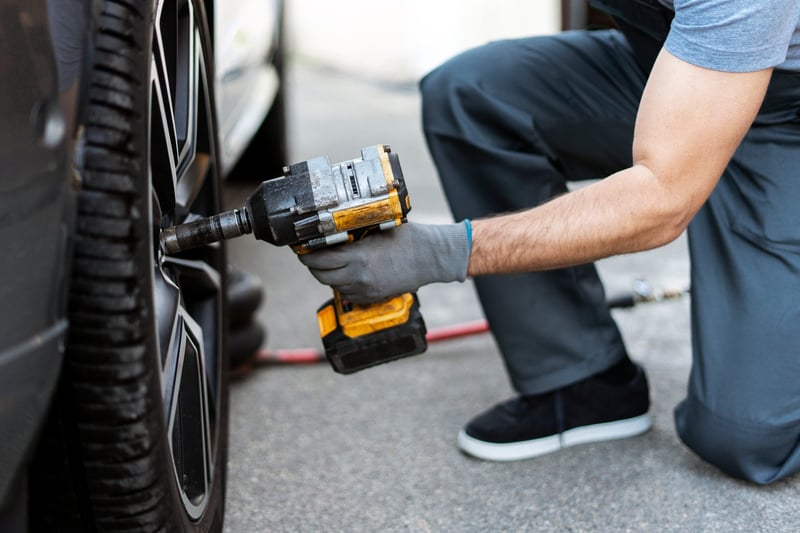 Mechanic is changing a car tire using a battery powered impact wrench in a repair shop
