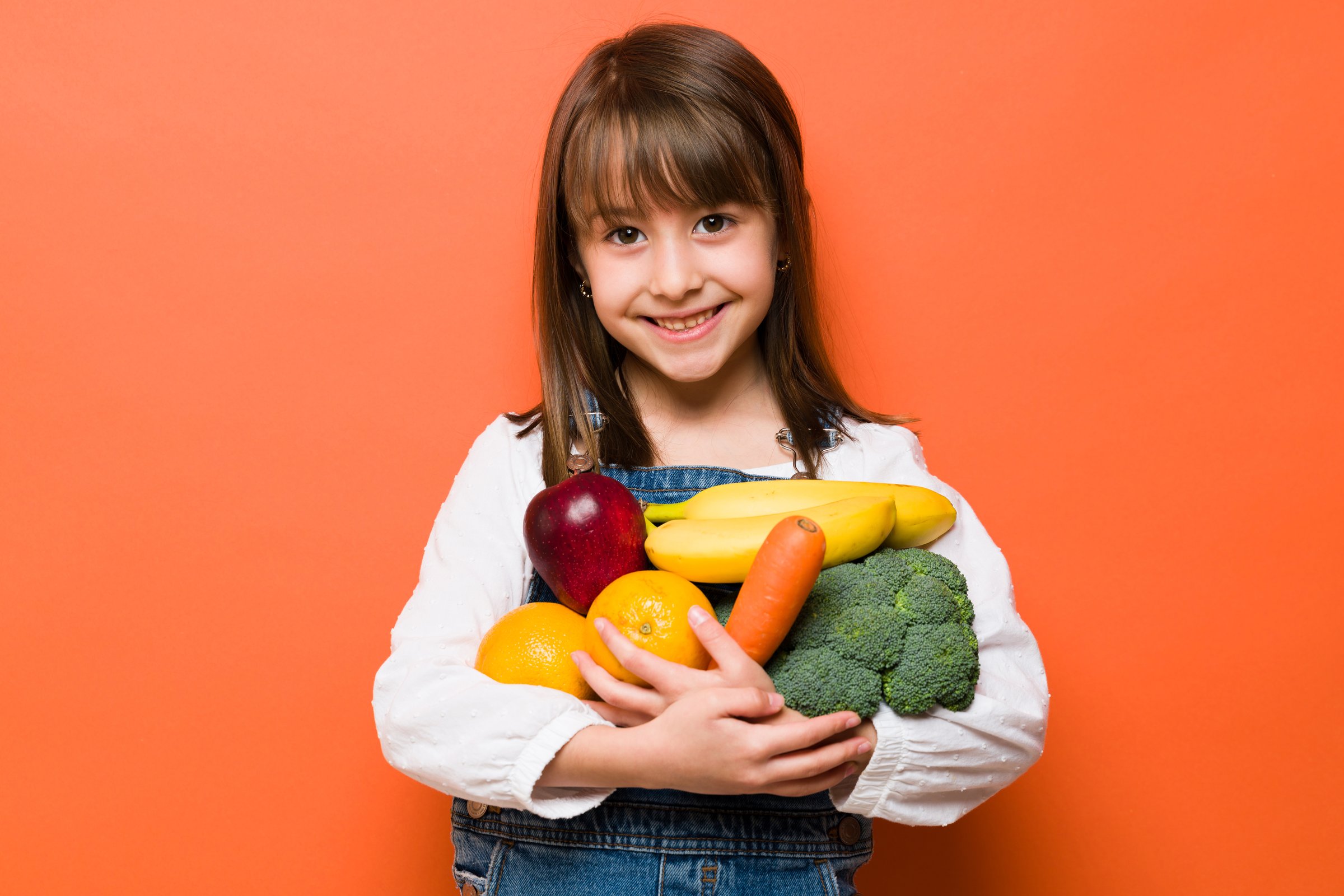Portrait of a beautiful little girl carrying a lot of fruits and vegetables and looking happy about healthy food