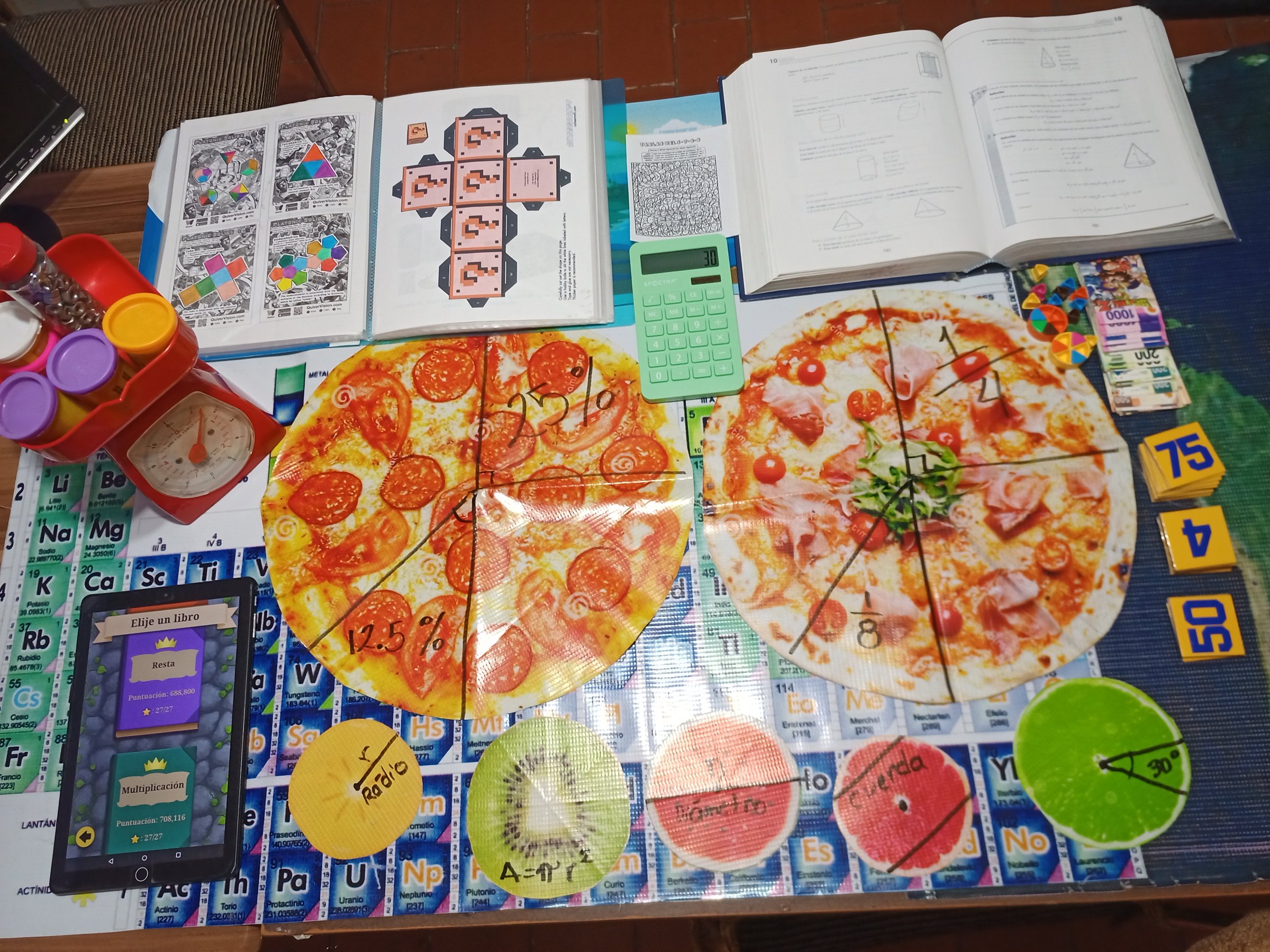 Math study setup with pizza-themed learning aids, calculator, textbooks, and periodic table placemat on a table.