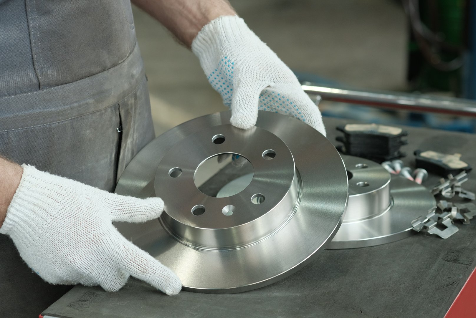 An auto mechanic checks the suspension elements of the car before installation. A new brake disc and a set of brake pads are on the desktop.