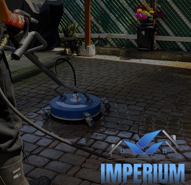 Person using a circular power washer on a cobblestone path, with "Imperium" logo on the lower right corner.