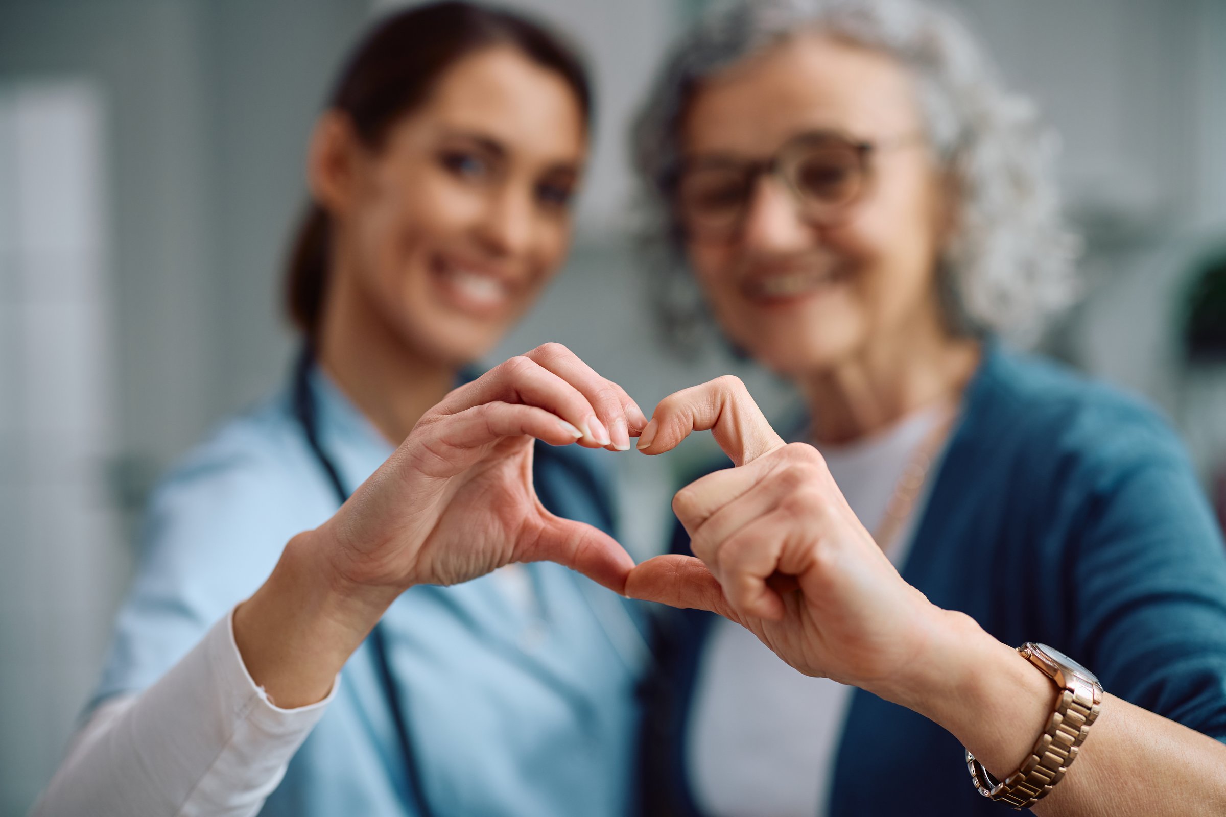 Close up of nurse and senior woman making heart shape with hands during a home visit.