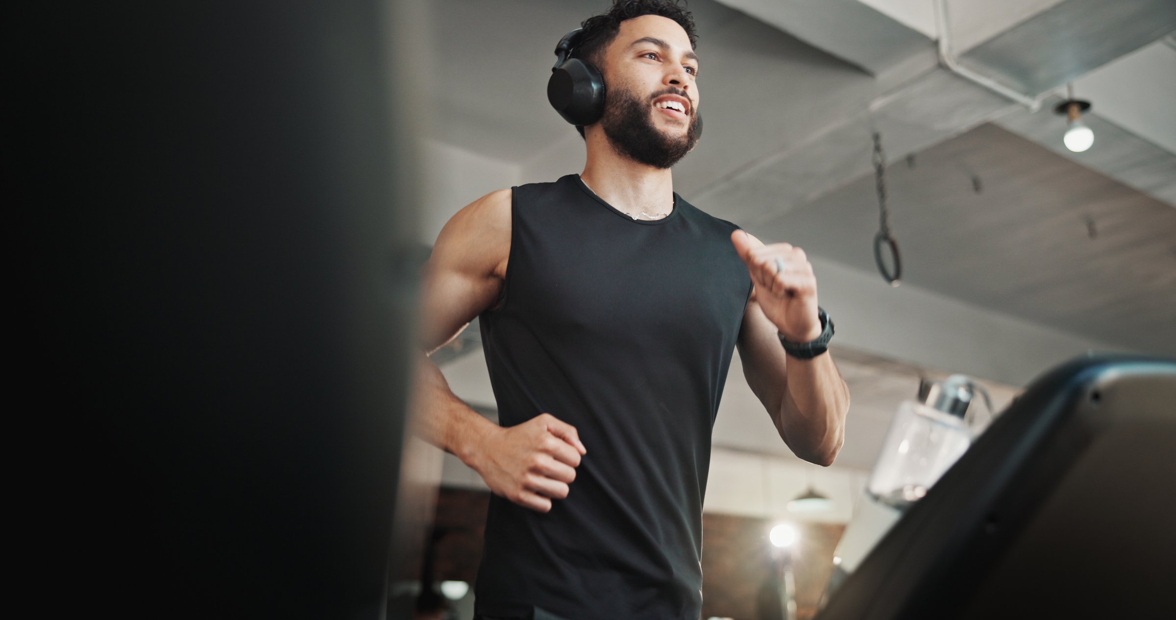 Man, headphones and running on treadmill at gym for exercise, training and cardio workout. Fitness, happy athlete and listening to music or radio on machine for marathon endurance and speed challenge