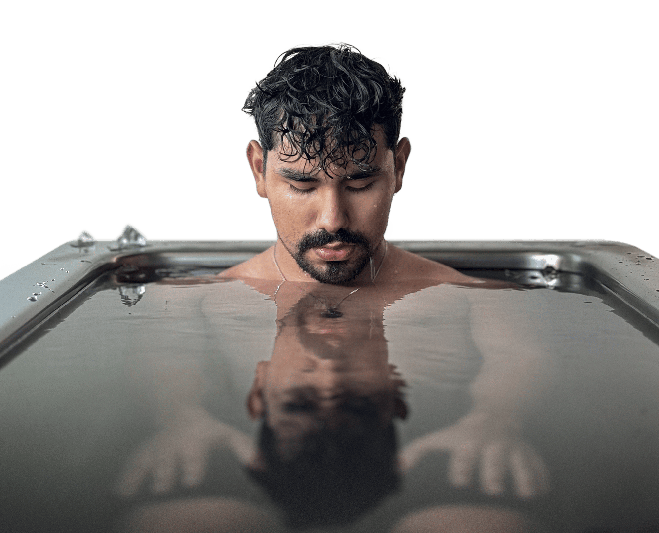 A person with a beard sits in a reflective water-filled bathtub, focusing intently, with a neutral background.