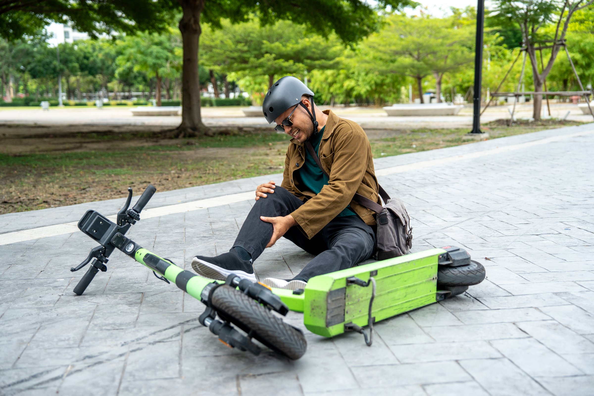 Young Asian Businessman falling off EV scooter on the road. Accident Injury leg pain. Broken leg falls off the Scooter. Accident on the road.