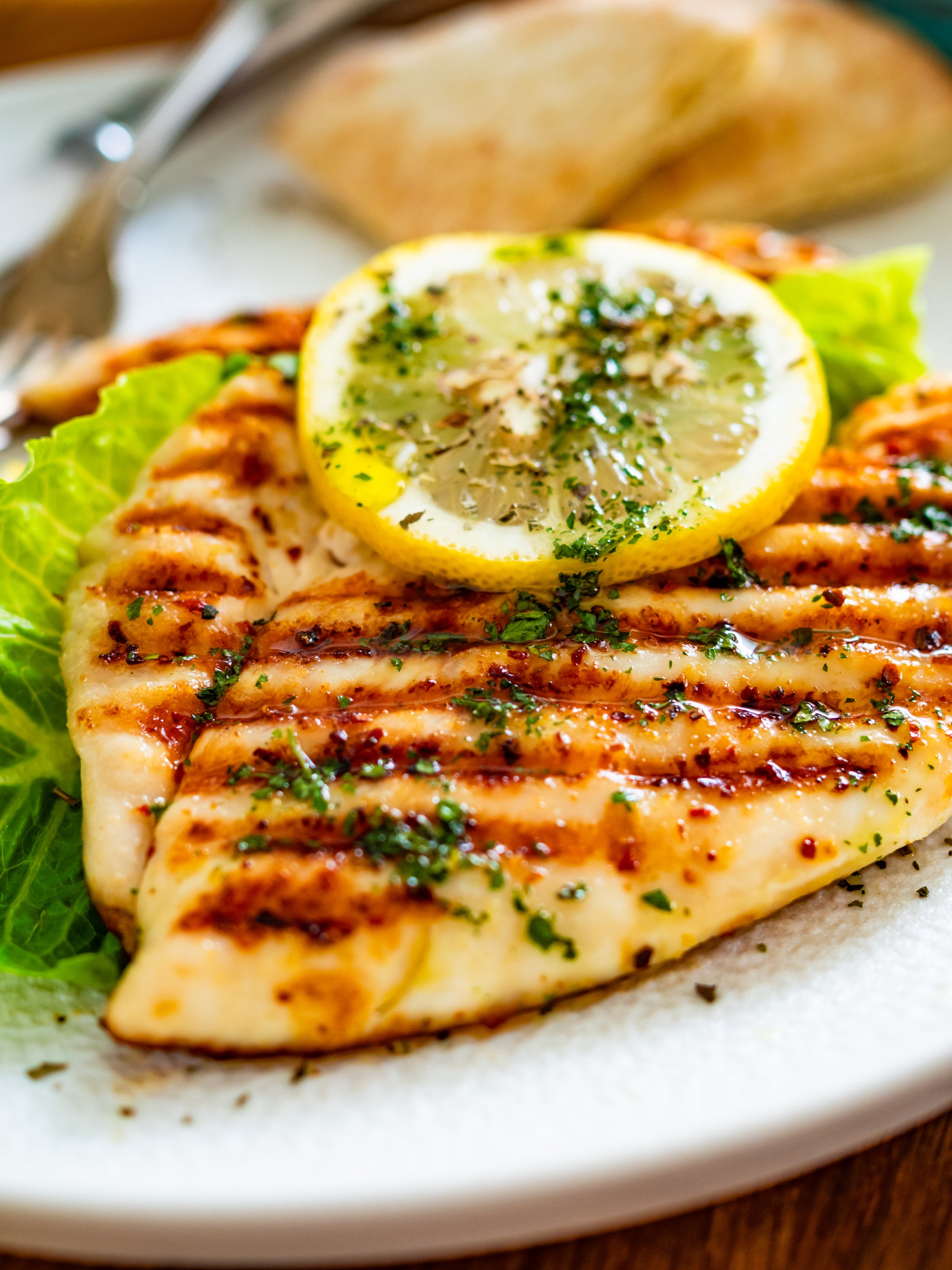Grilled chicken breast, pita bread and tzatziki served on black stony board on wooden table