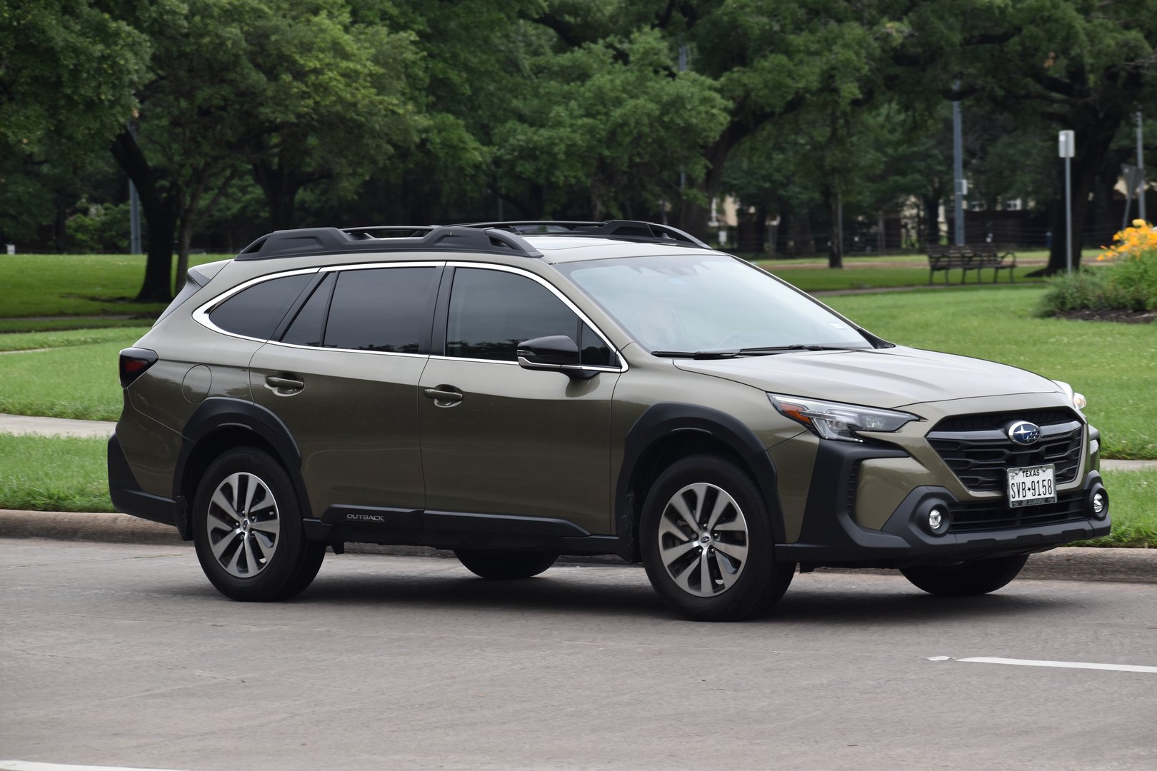 Houston, Texas USA - Hermann Park, Summer 4/29/2023 - Portrait of an olive-green colored Subaru Outback cruising through a nature reserve
